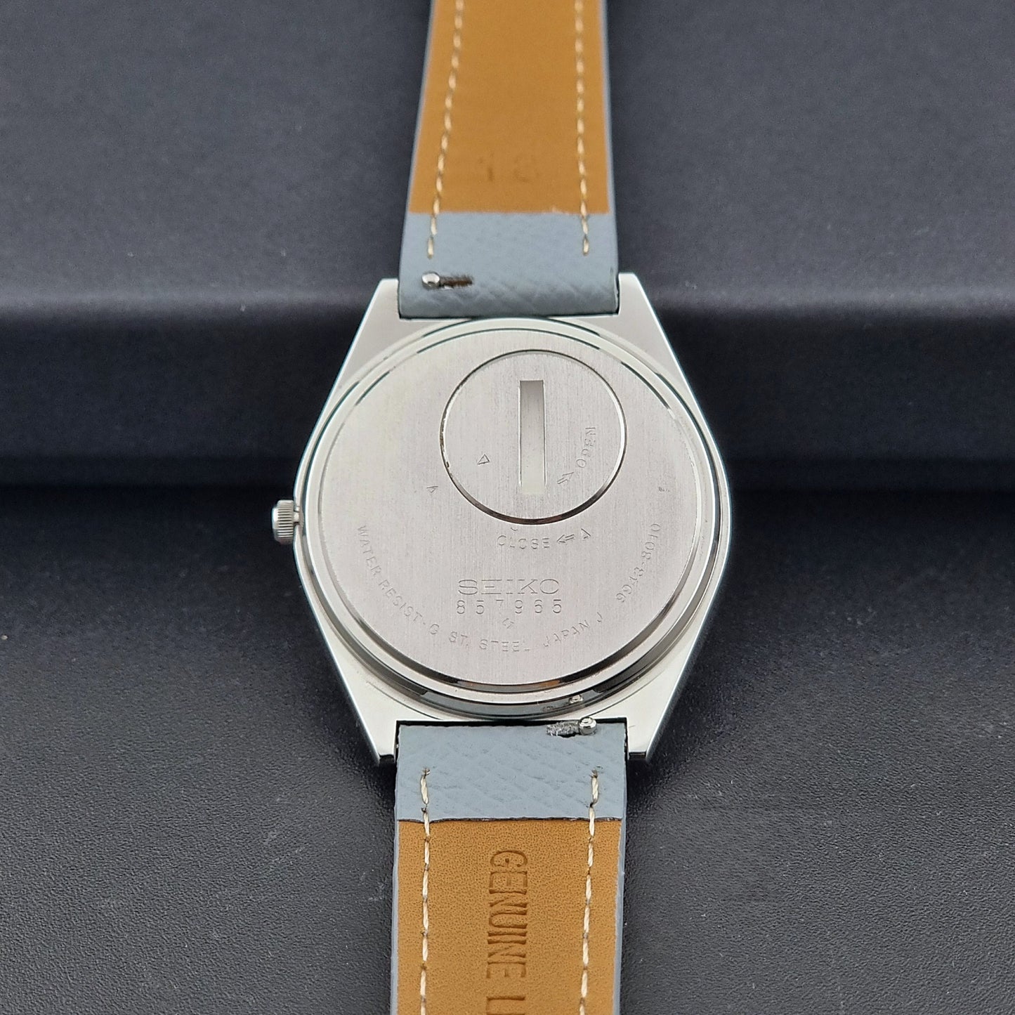 Vintage Seiko Grand Quartz Wristwatch 9943-8010 with grey strap on a dark gray background case back view