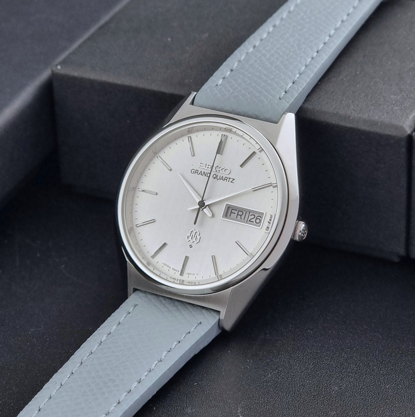 Vintage Seiko Grand Quartz Wristwatch 9943-8010 with grey strap on a dark gray background crown view
