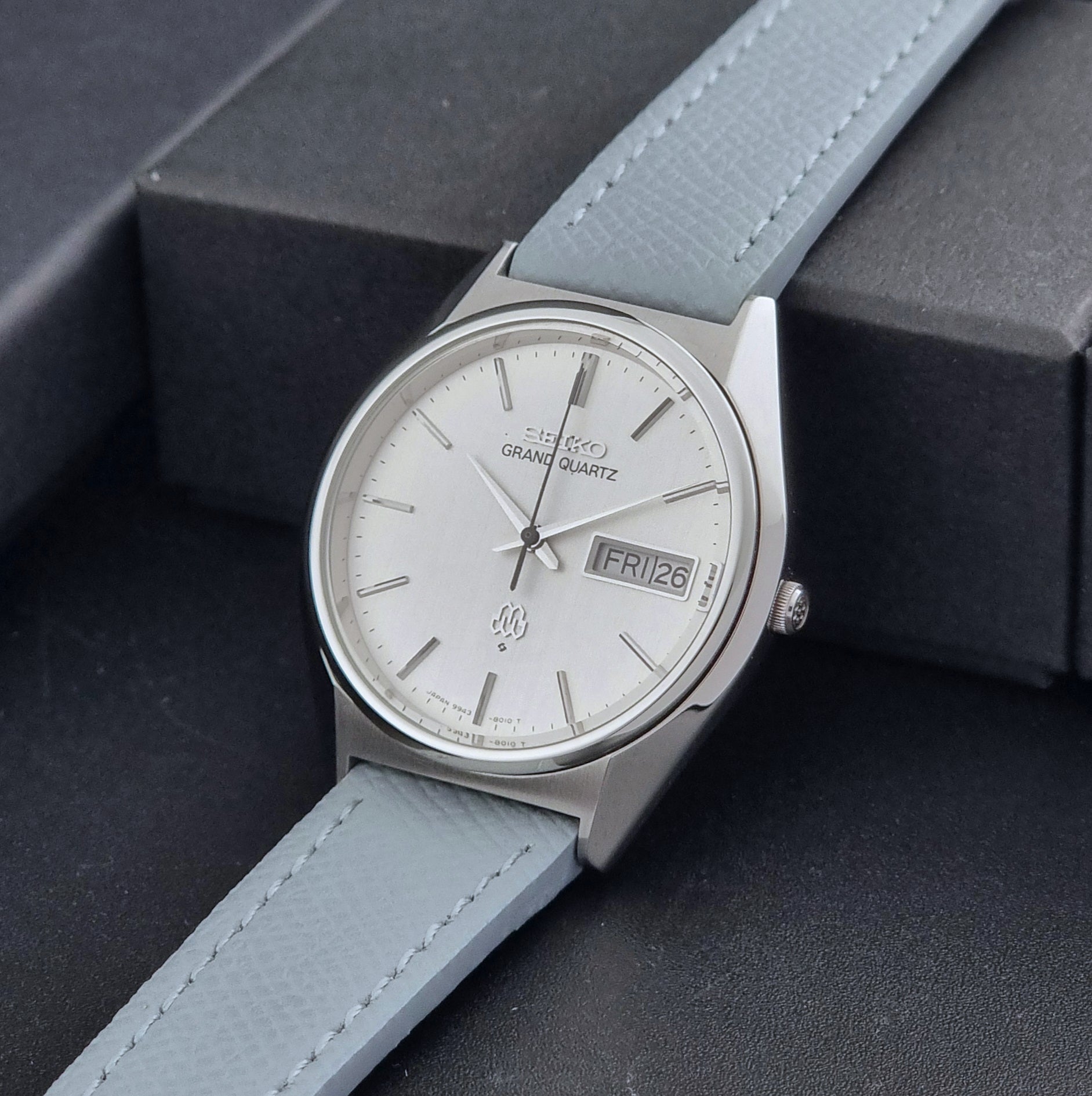 Vintage Seiko Grand Quartz Wristwatch 9943-8010 with grey strap on a dark gray background crown view