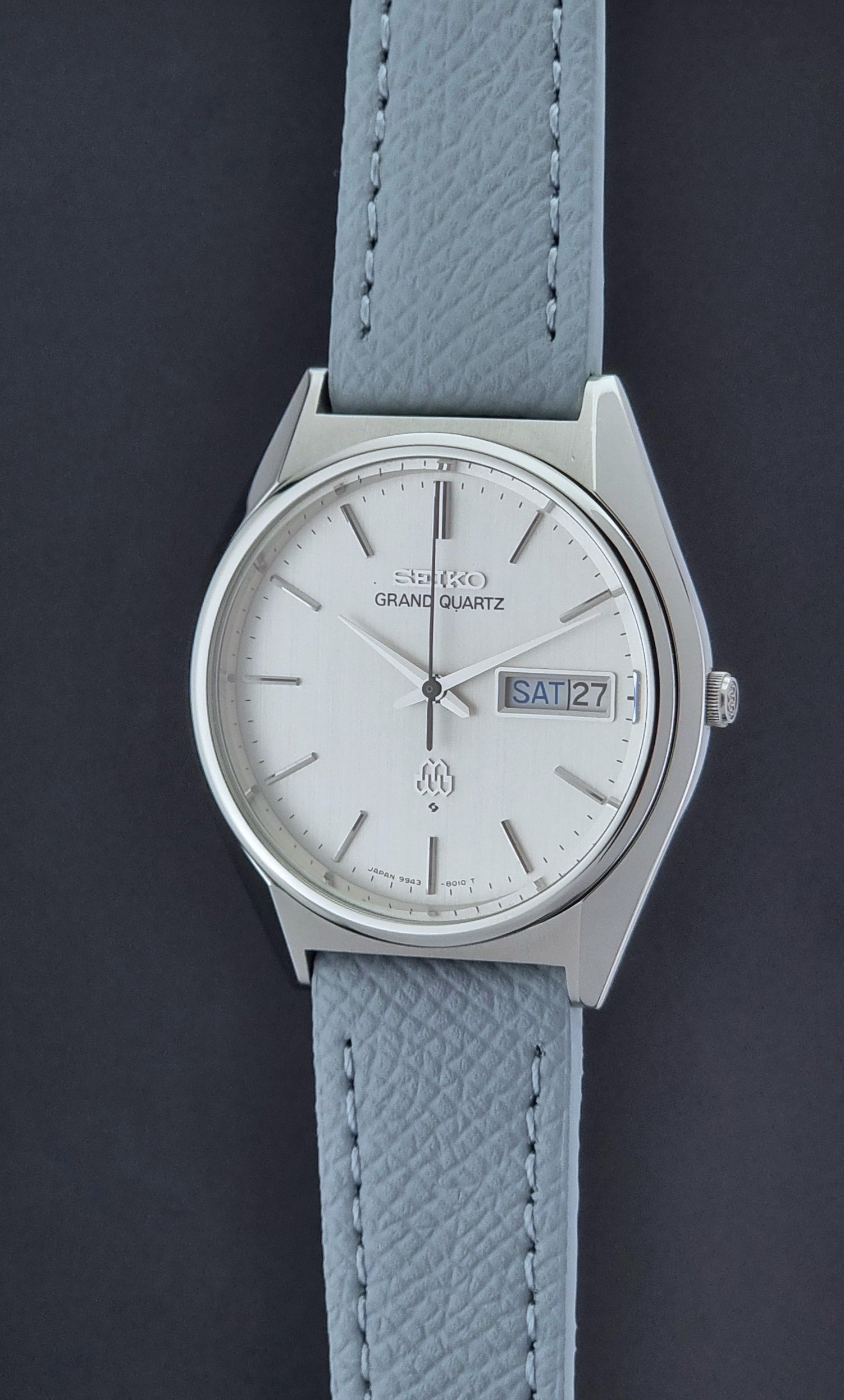 Vintage Seiko Grand Quartz Wristwatch 9943-8010 with grey strap on a dark gray background crown profile view