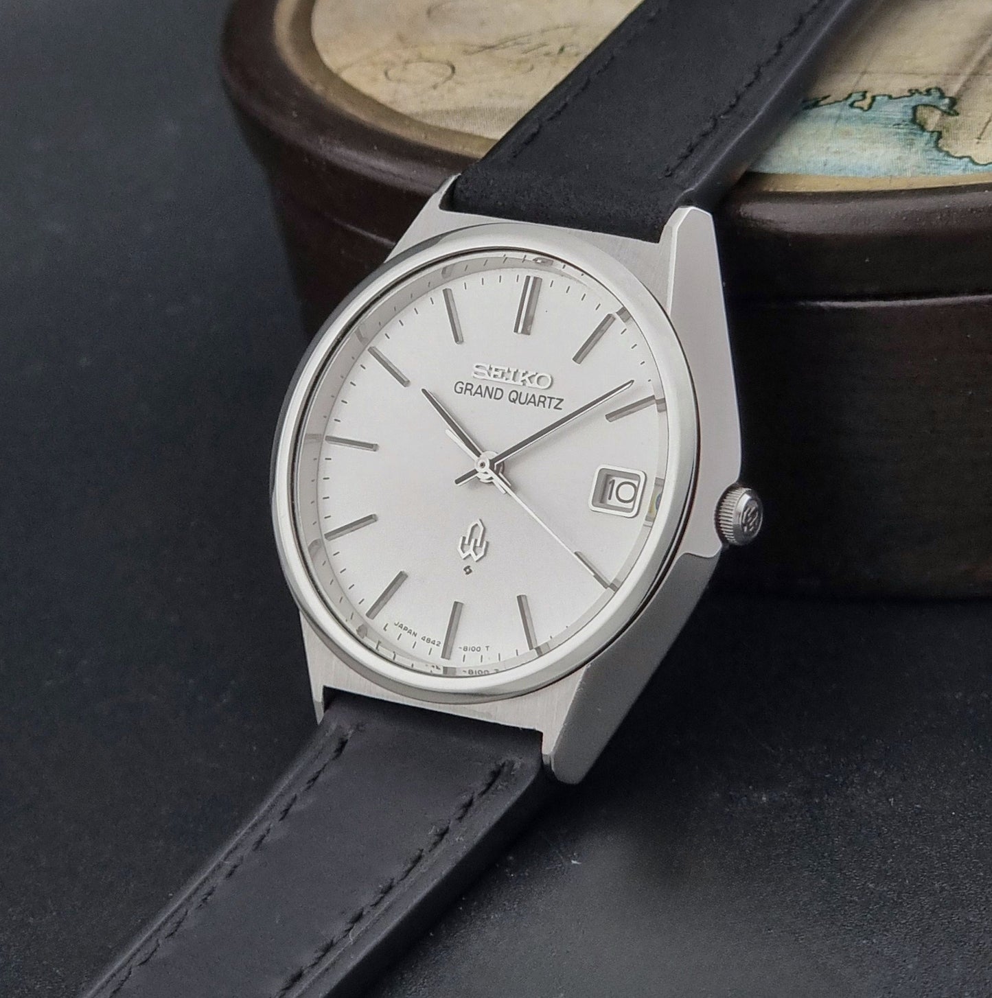 Vintage Seiko Grand Quartz watch 4842-8110 with a silver case and black leather strap on a dark gray background crown view