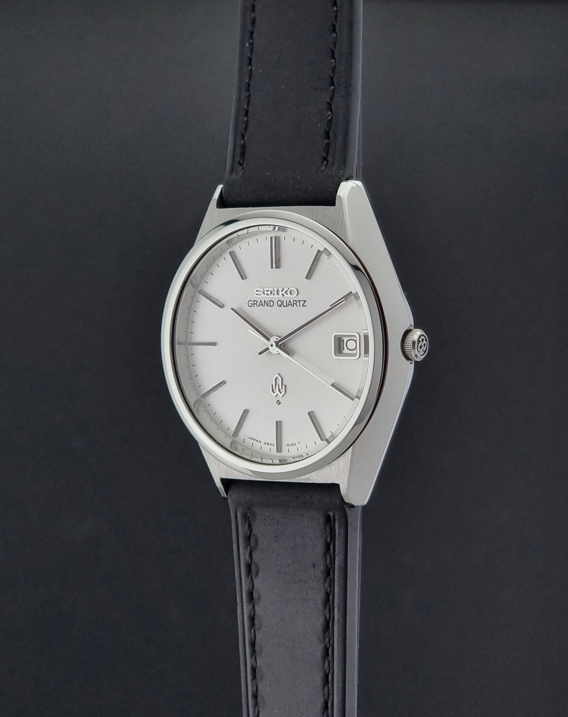 Vintage Seiko Grand Quartz watch 4842-8110 with a silver case and black leather strap on a dark gray background crown profile view