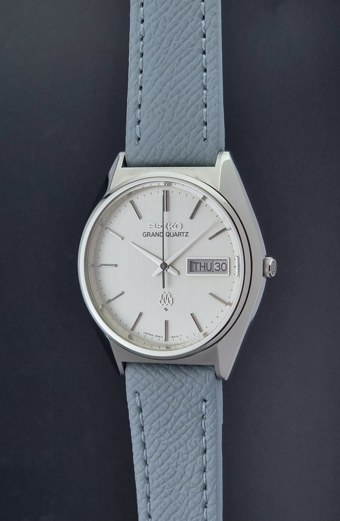 Vintage Seiko Grand Quartz 9943-8010 with a light grey strap on a dark background crown profiel view