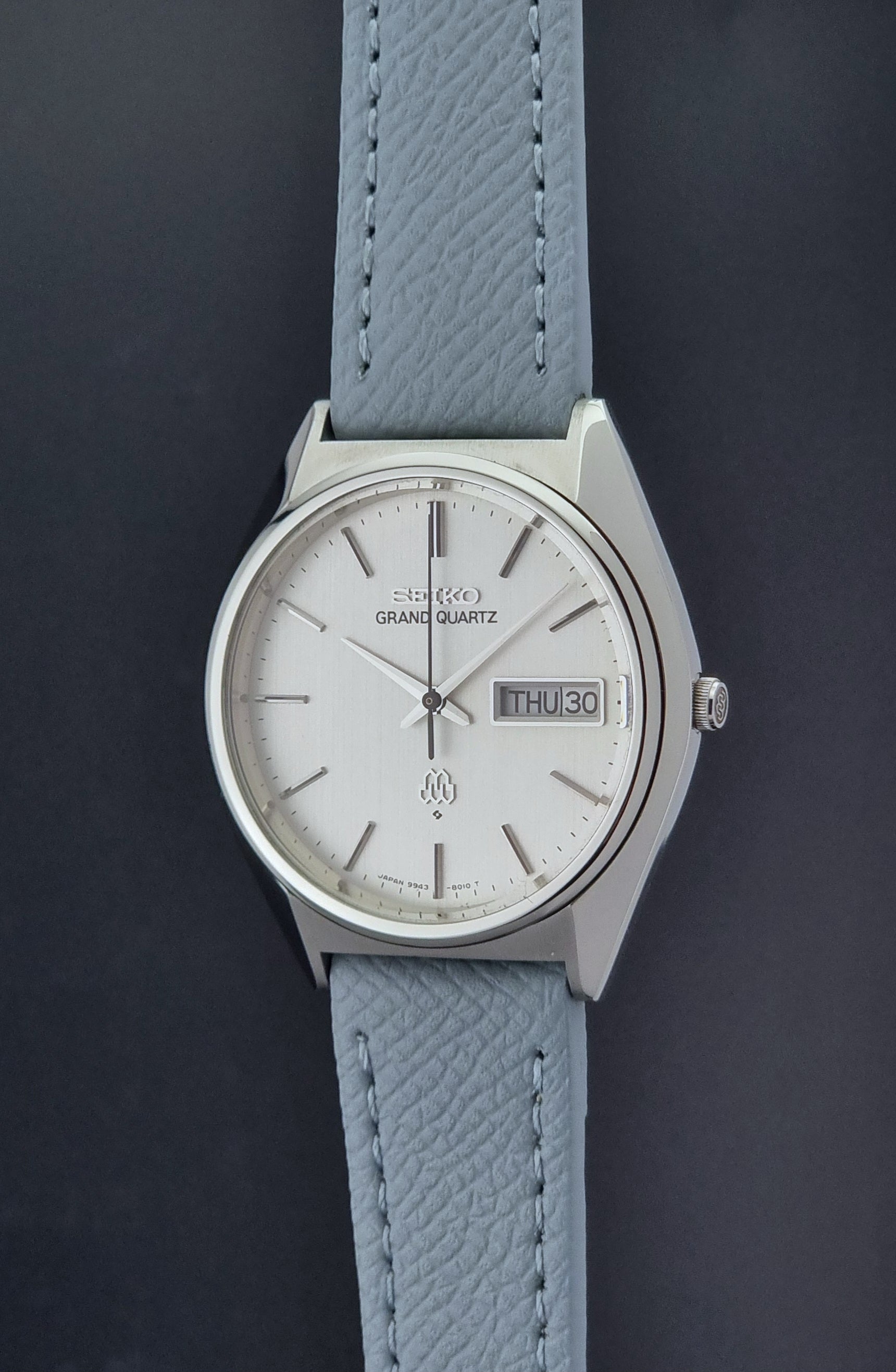Vintage Seiko Grand Quartz 9943-8010 with a light grey strap on a dark background crown profiel view