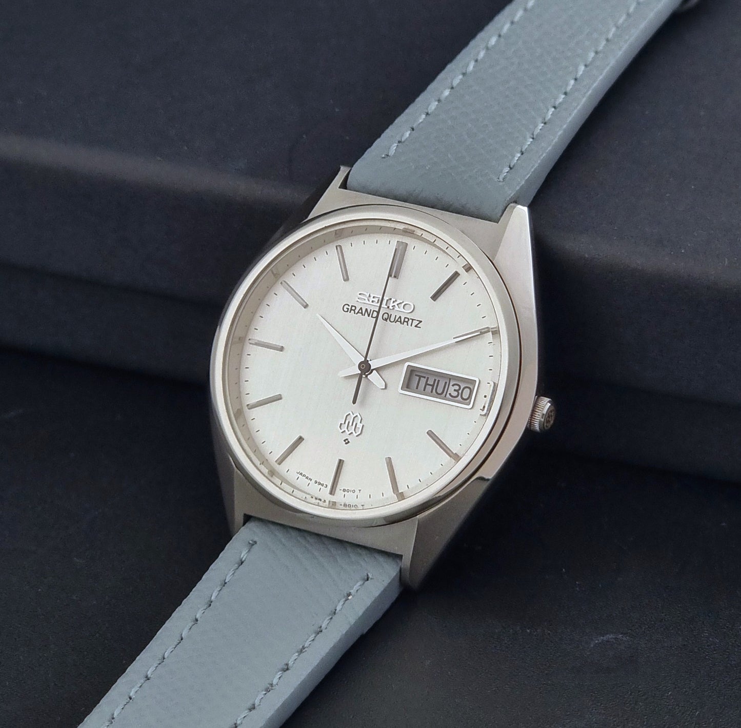 Vintage Seiko Grand Quartz 9943-8010 with a light grey strap on a dark background crown view