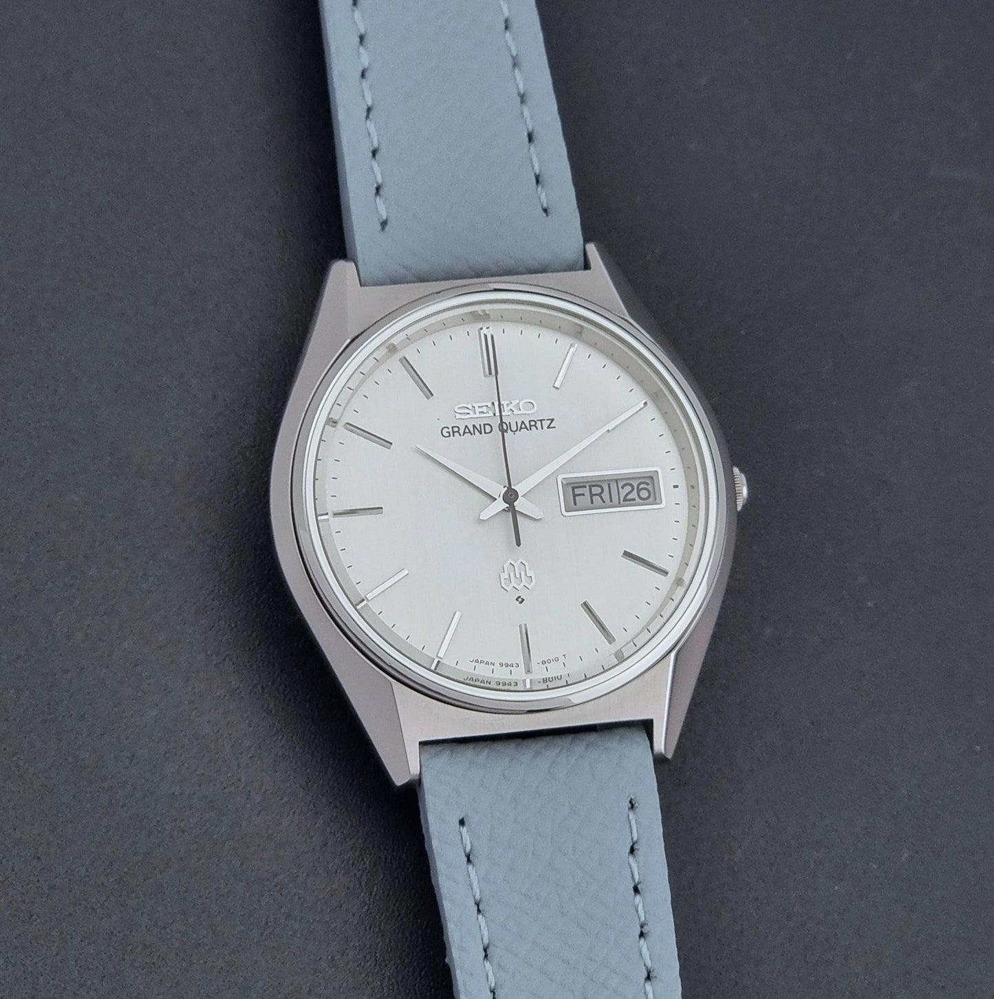 Vintage Seiko Grand Quartz Wristwatch 9943-8010 with grey strap on a dark gray background front view
