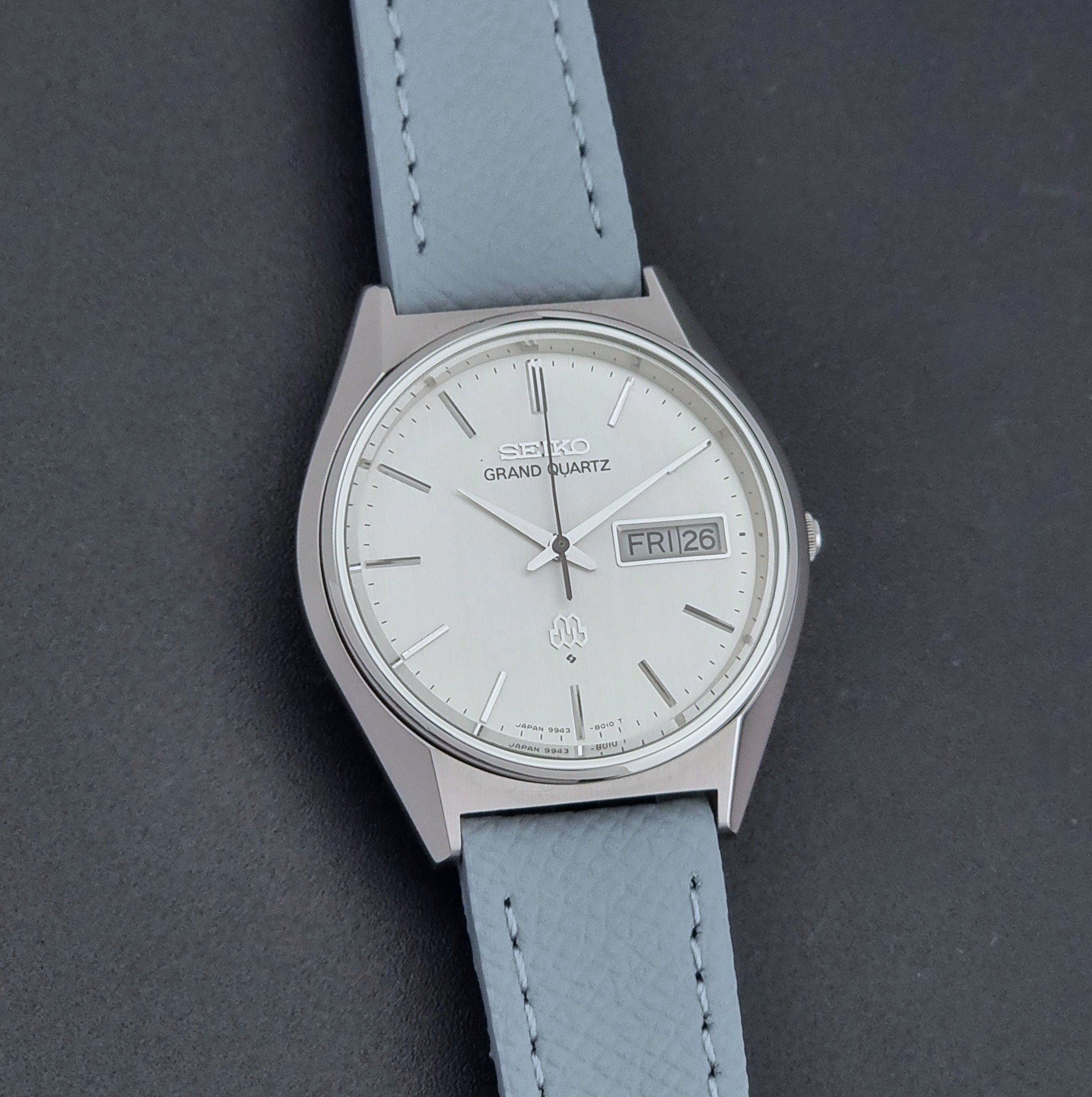 Vintage Seiko Grand Quartz Wristwatch 9943-8010 with grey strap on a dark gray background front view