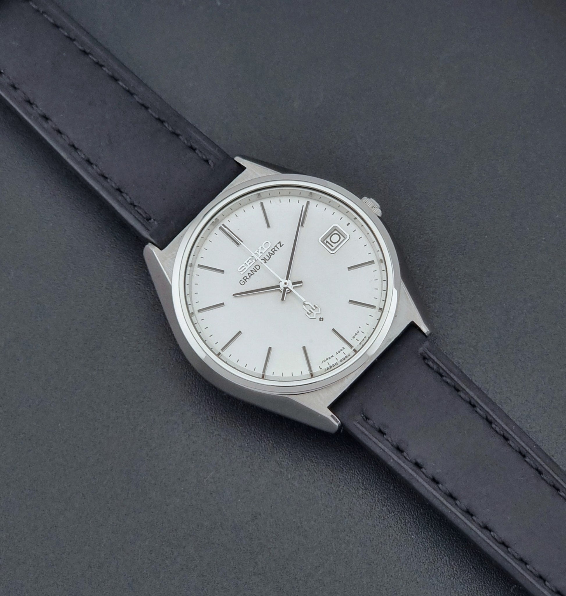 Vintage Seiko Grand Quartz watch 4842-8110 with a silver case and black leather strap on a dark gray background dial 