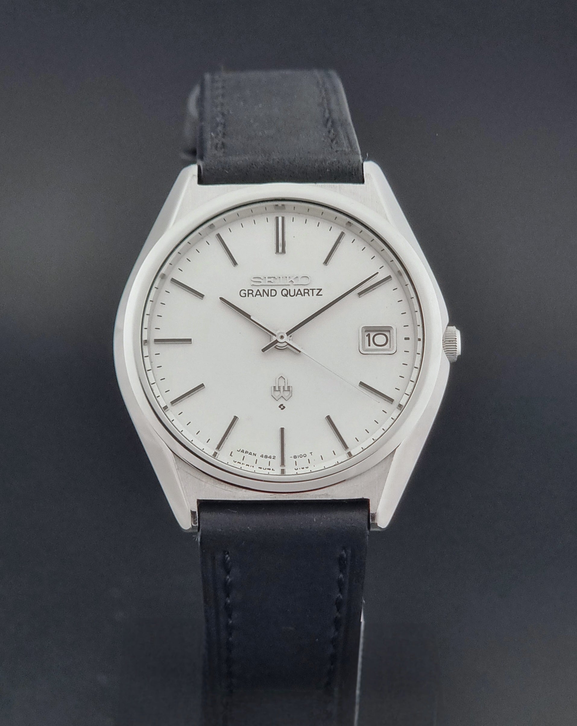 Vintage Seiko Grand Quartz watch 4842-8110 with a silver case and black leather strap on a dark gray background close dial view