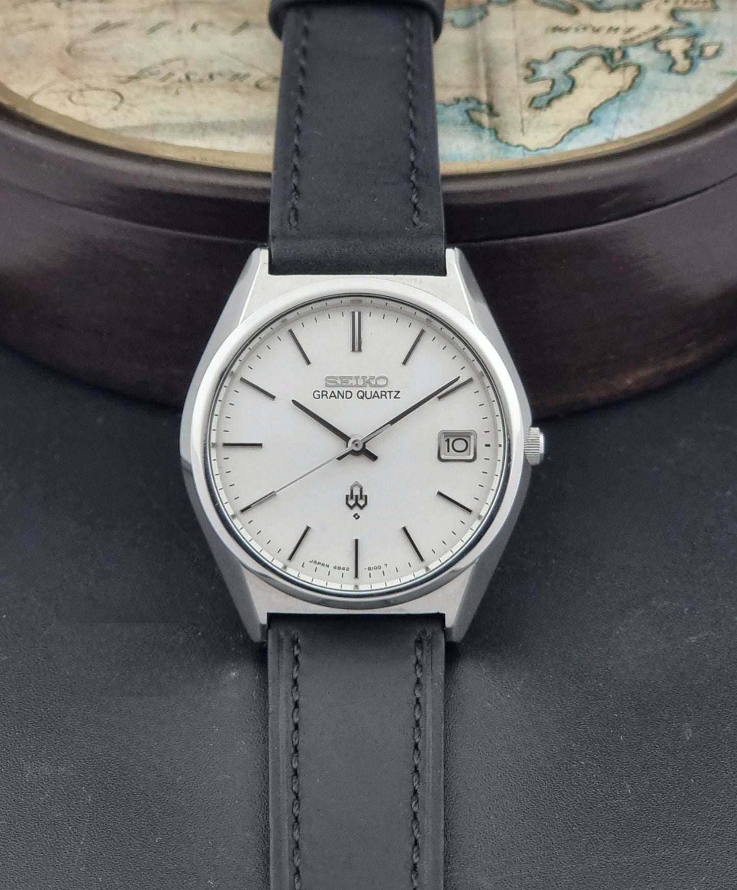 Vintage Seiko Grand Quartz watch 4842-8110 with a silver case and black leather strap on a dark gray background dial view