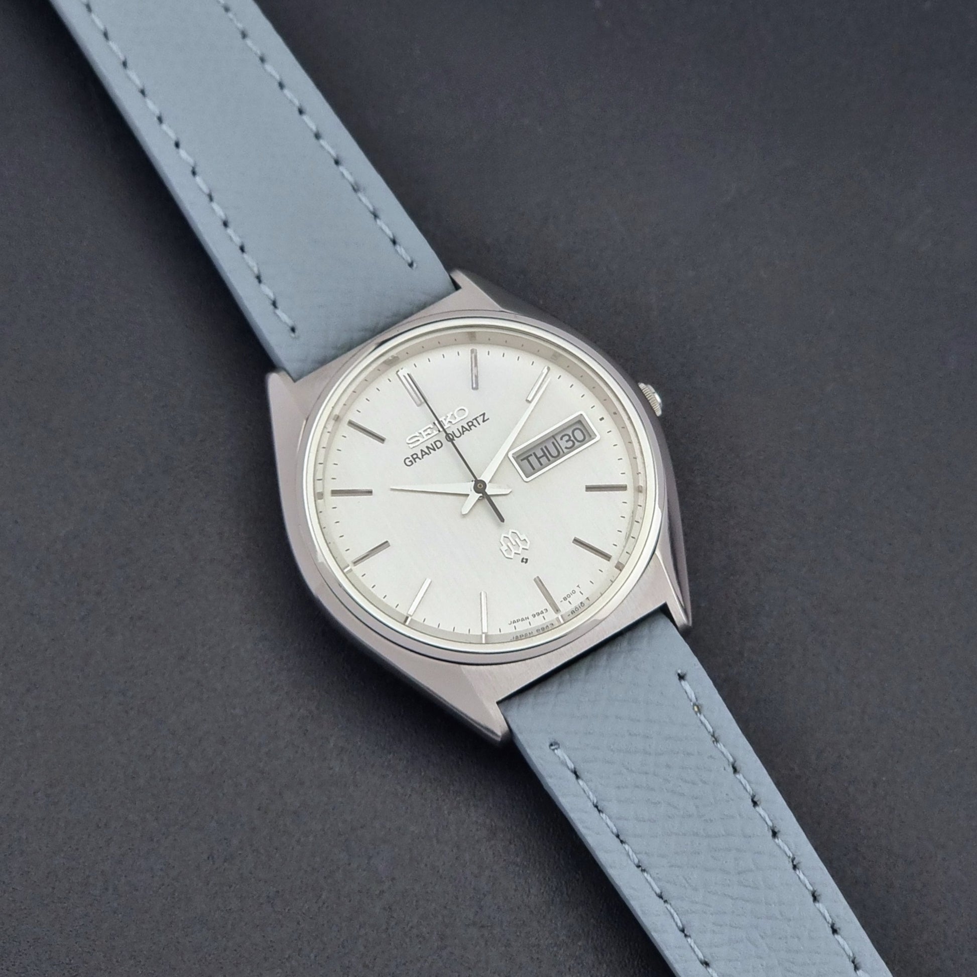 Vintage Seiko Grand Quartz 9943-8010 with a light grey strap on a dark background close up dial view