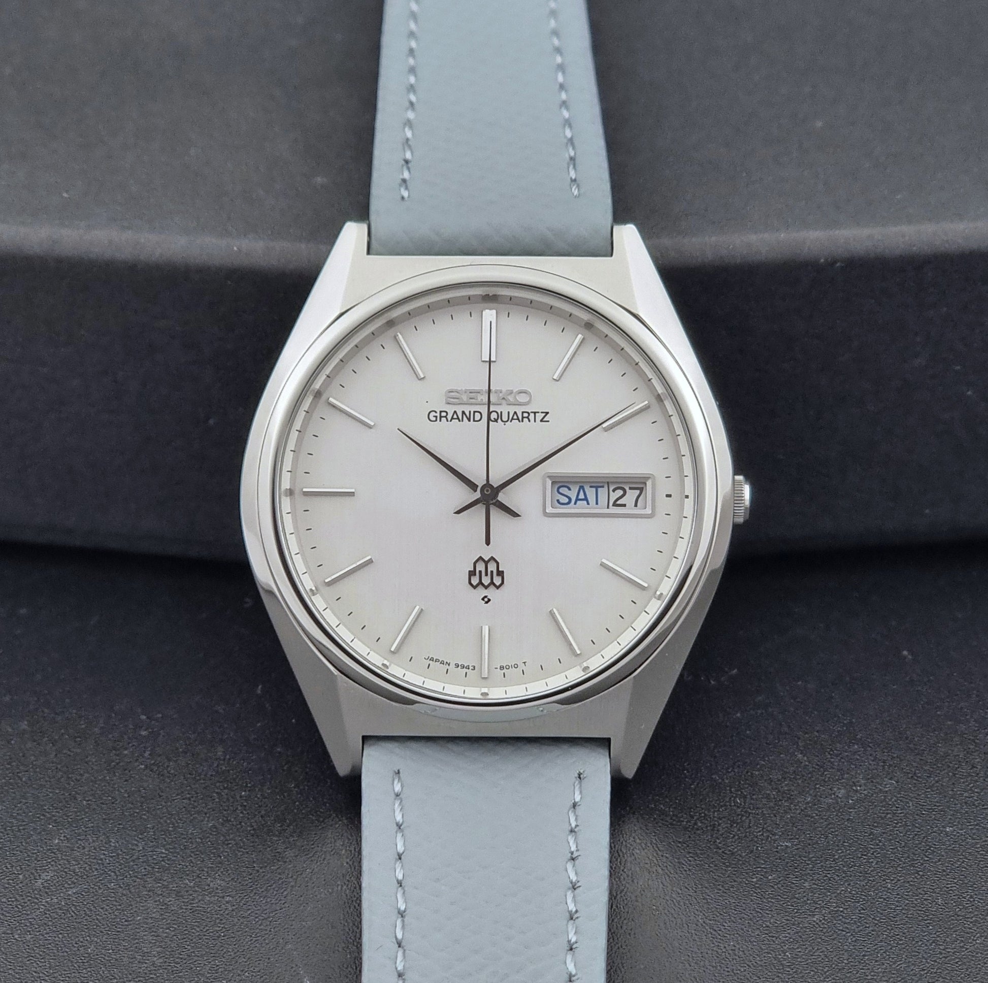 Vintage Seiko Grand Quartz Wristwatch 9943-8010 with grey strap on a dark gray background front view