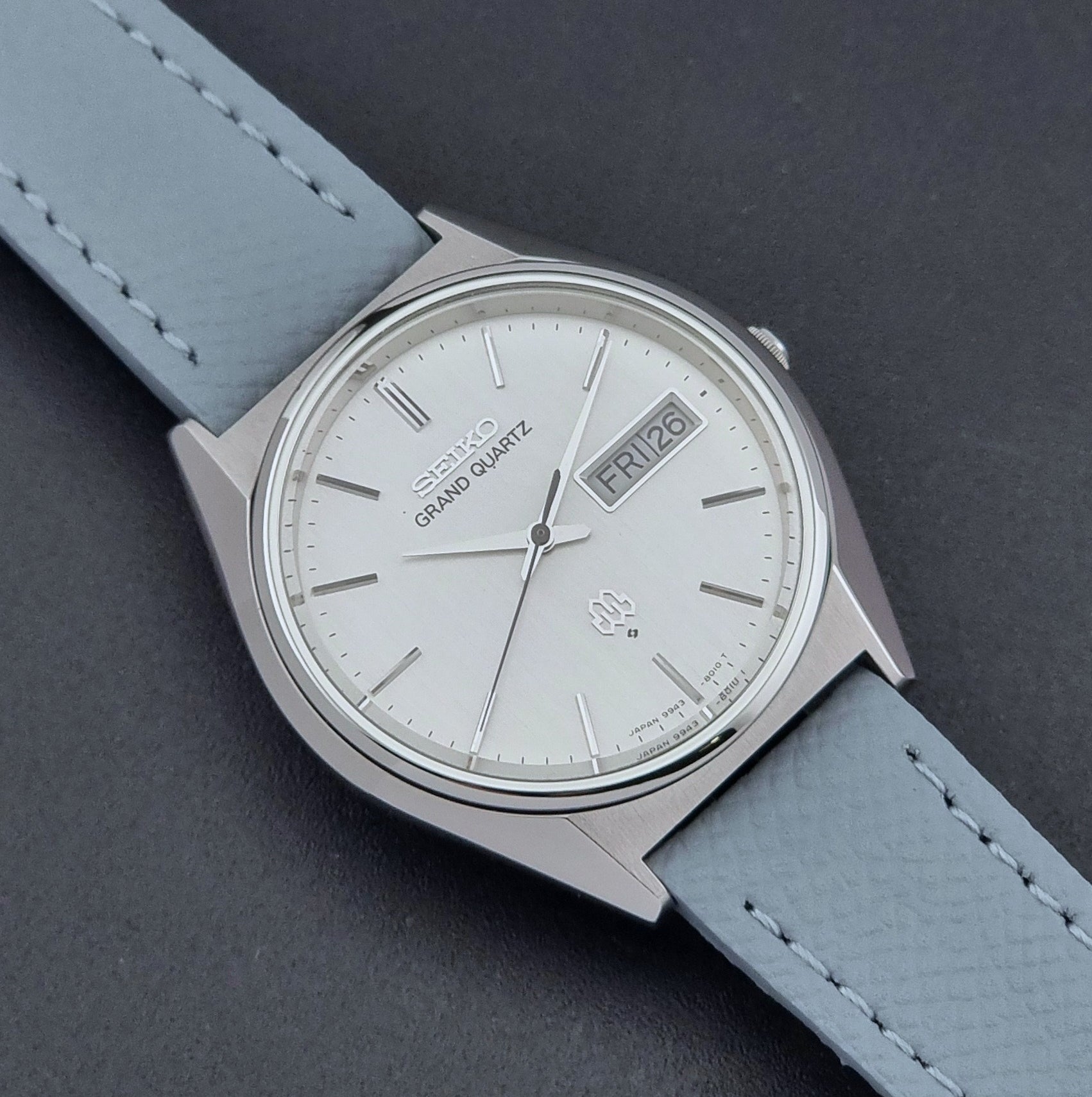 Vintage Seiko Grand Quartz Wristwatch 9943-8010 with grey strap on a dark gray background close up dial view