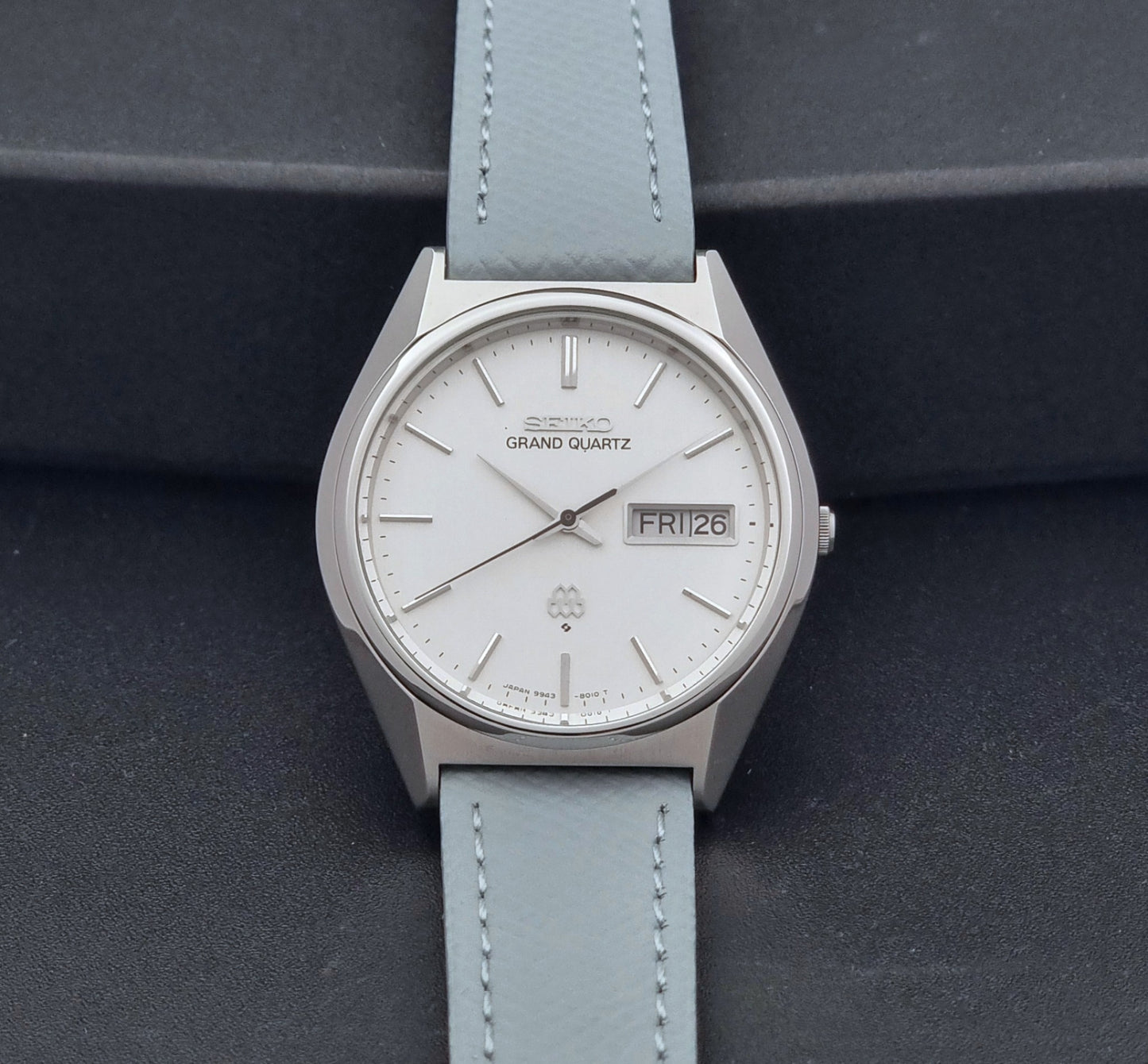 Vintage Seiko Grand Quartz Wristwatch 9943-8010 with grey strap on a dark gray background dial view