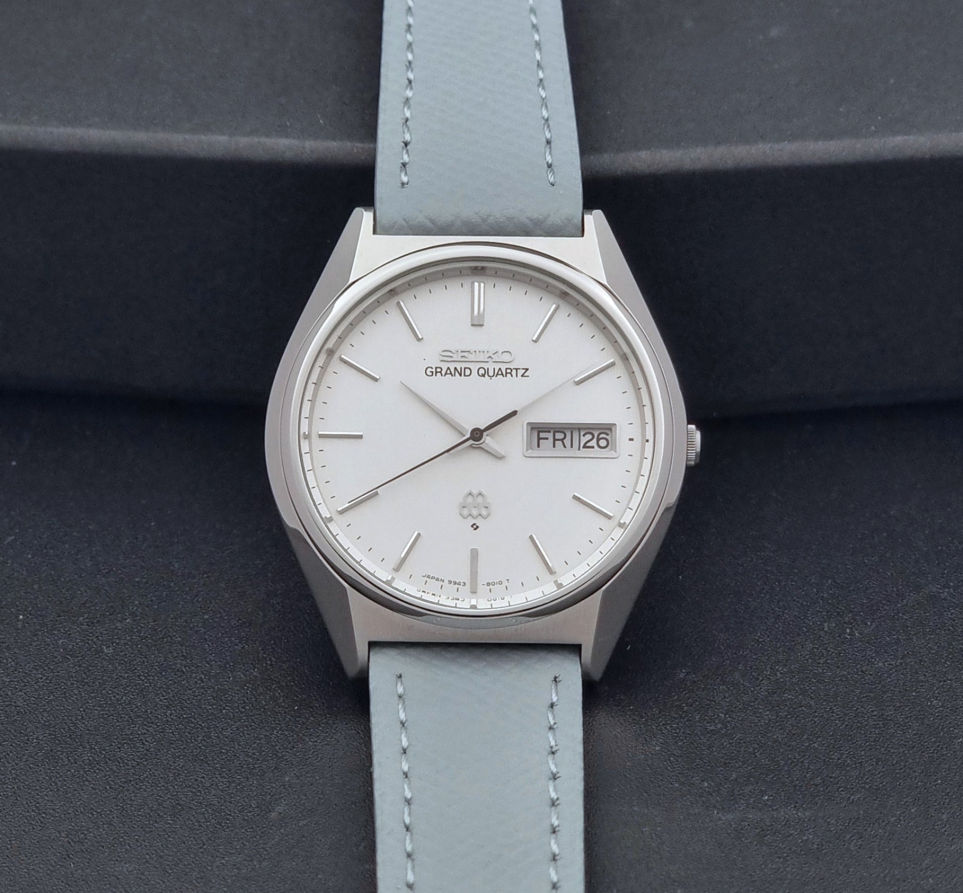 Vintage Seiko Grand Quartz Wristwatch 9943-8010 with grey strap on a dark gray background dial view