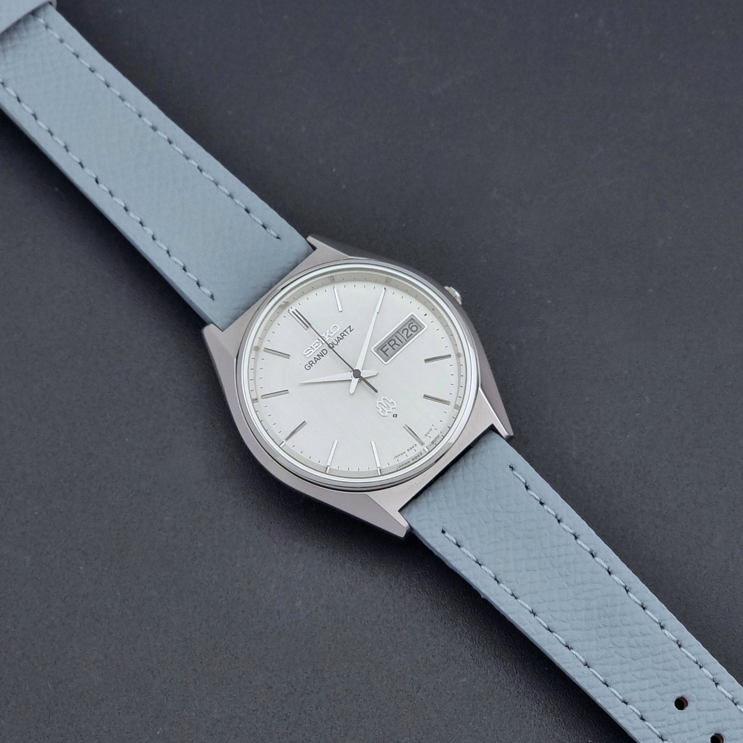 Vintage Seiko Grand Quartz Wristwatch 9943-8010 with grey strap on a dark gray background dial