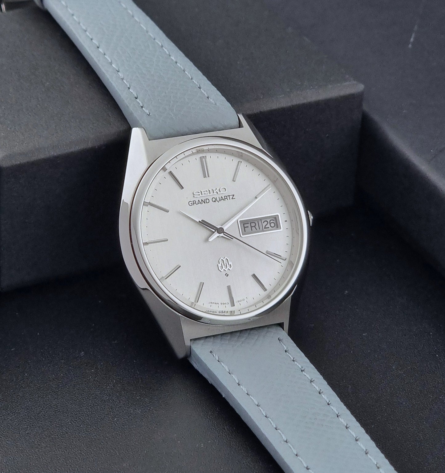 Vintage Seiko Grand Quartz Wristwatch 9943-8010 with grey strap on a dark gray background side view