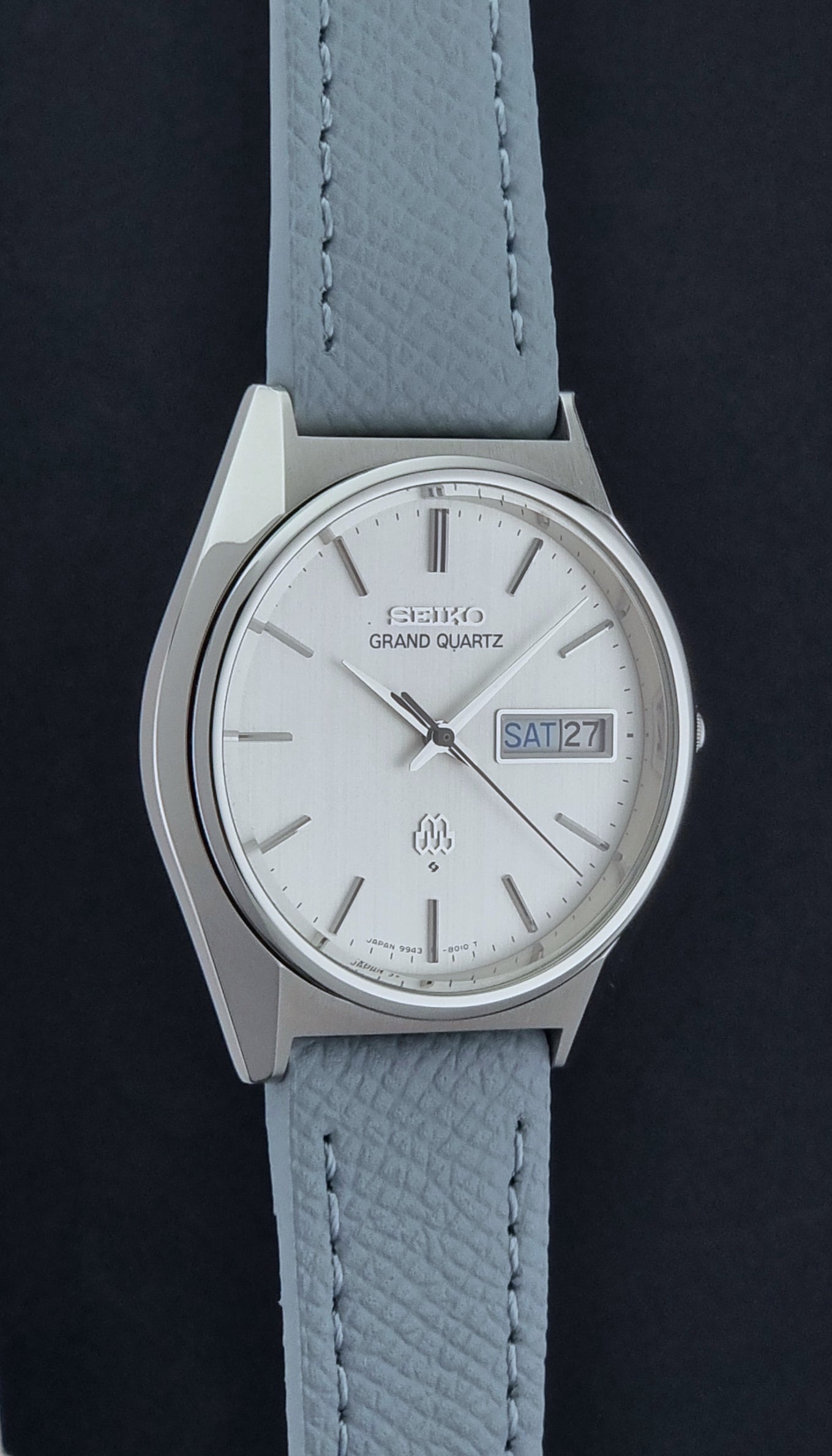 Vintage Seiko Grand Quartz Wristwatch 9943-8010 with grey strap on a dark gray background side profile view