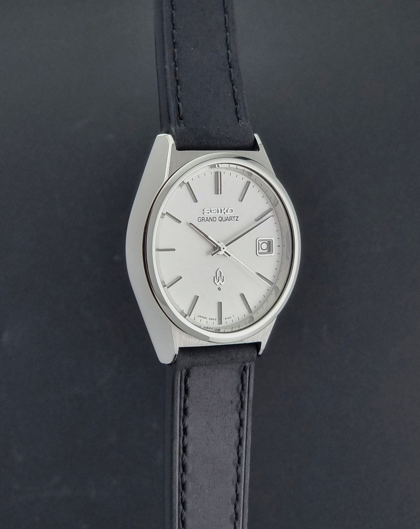 Vintage Seiko Grand Quartz watch 4842-8110 with a silver case and black leather strap on a dark gray background side profile view
