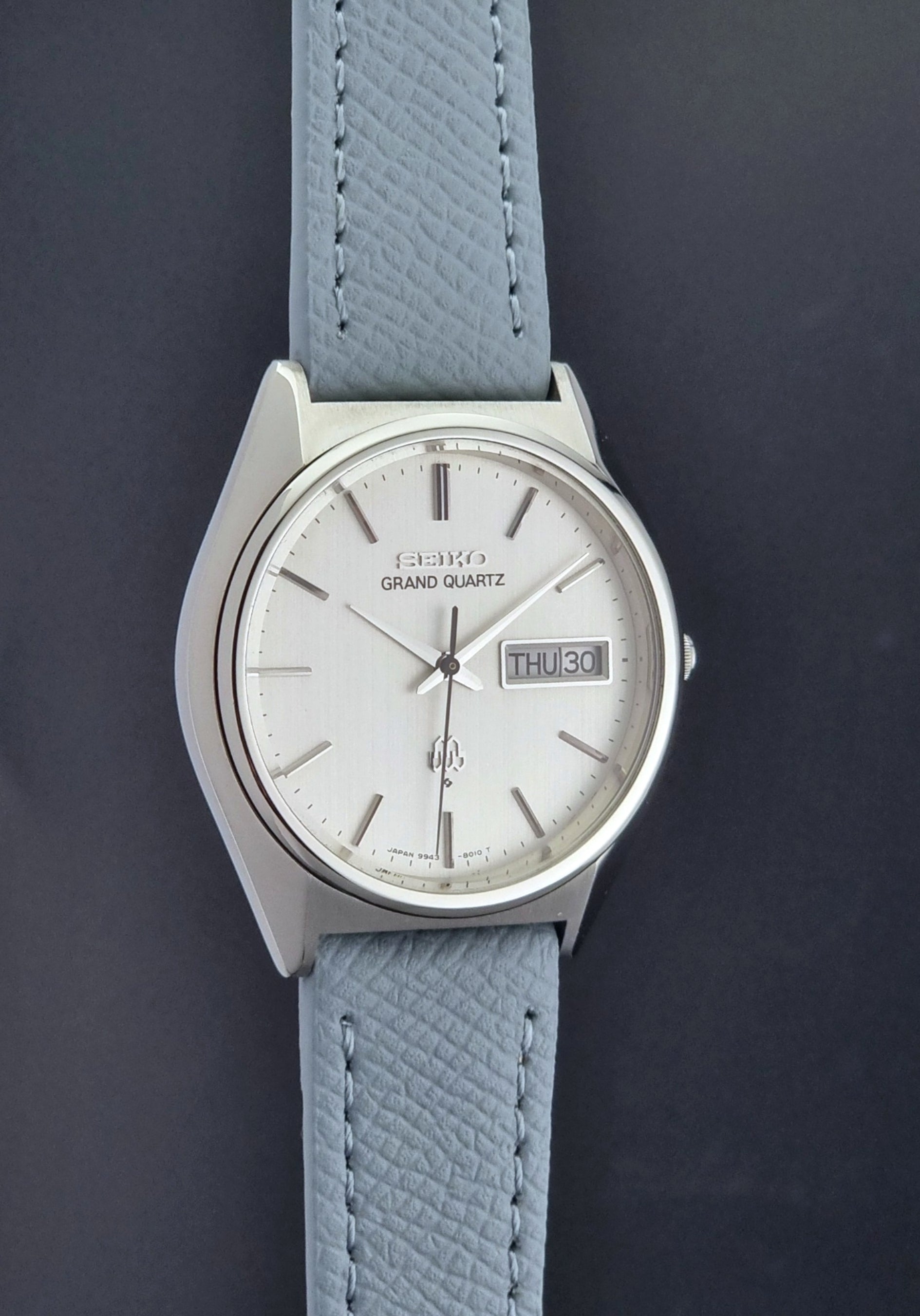 Vintage Seiko Grand Quartz 9943-8010 with a light grey strap on a dark background side profile view