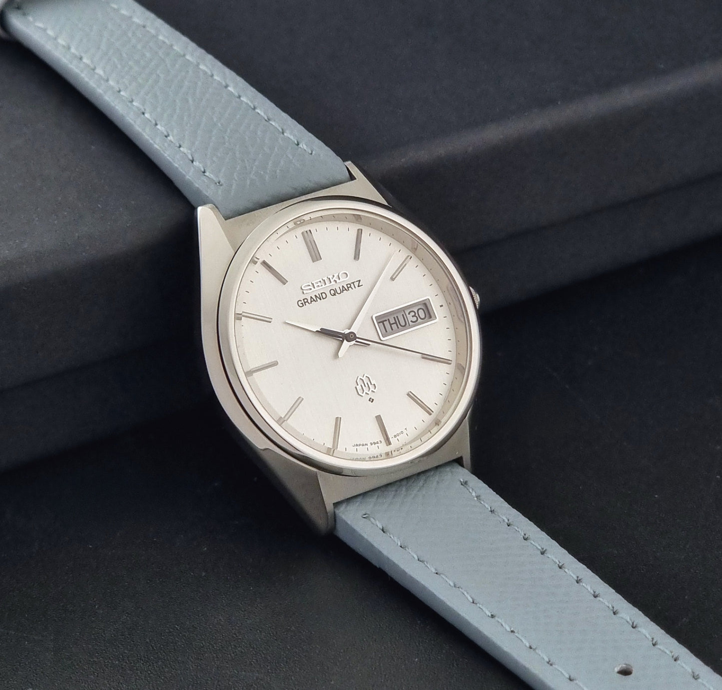 Vintage Seiko Grand Quartz 9943-8010 with a light grey strap on a dark background side view