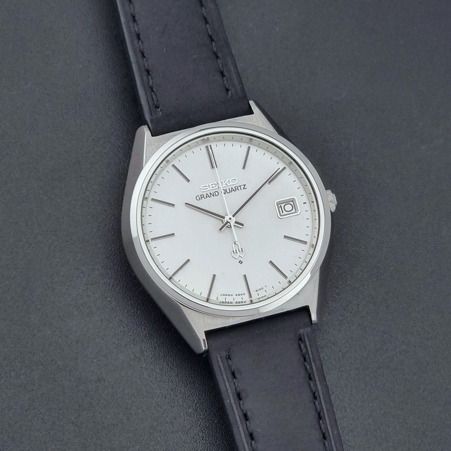 Vintage Seiko Grand Quartz watch 4842-8110 with a silver case and black leather strap on a dark gray background front view