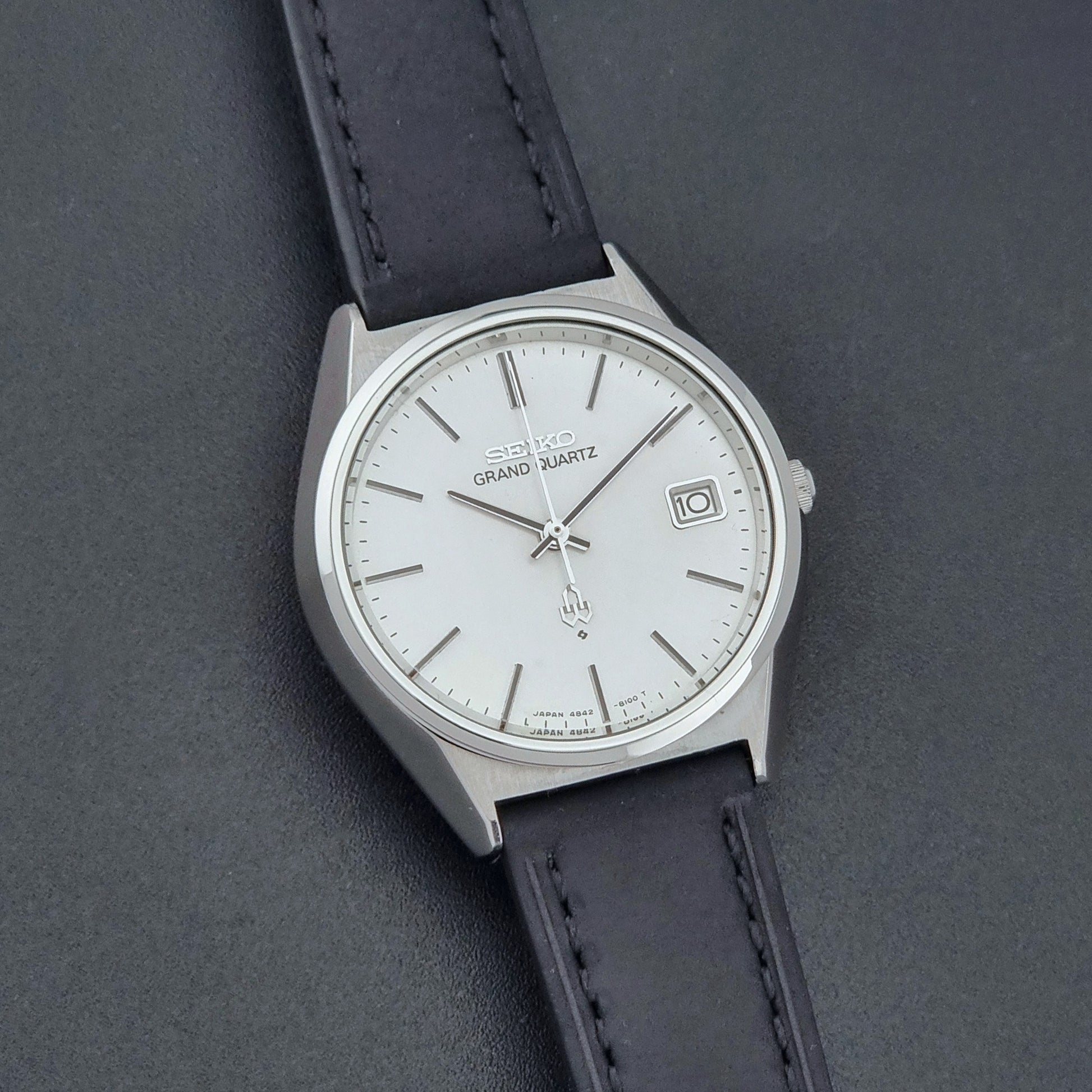 Vintage Seiko Grand Quartz watch 4842-8110 with a silver case and black leather strap on a dark gray background front view