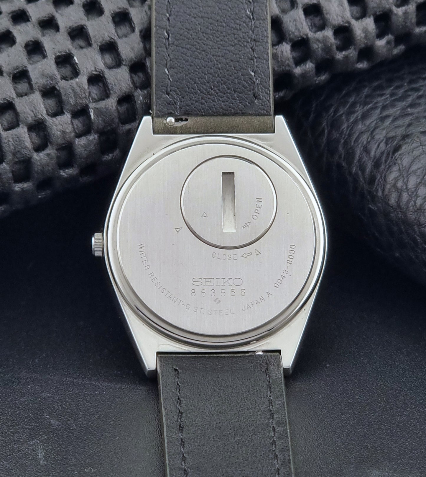 Vintage Seiko Grand Quartz watch 9943-8030 with gray leather strap on a dark gray background case back view
