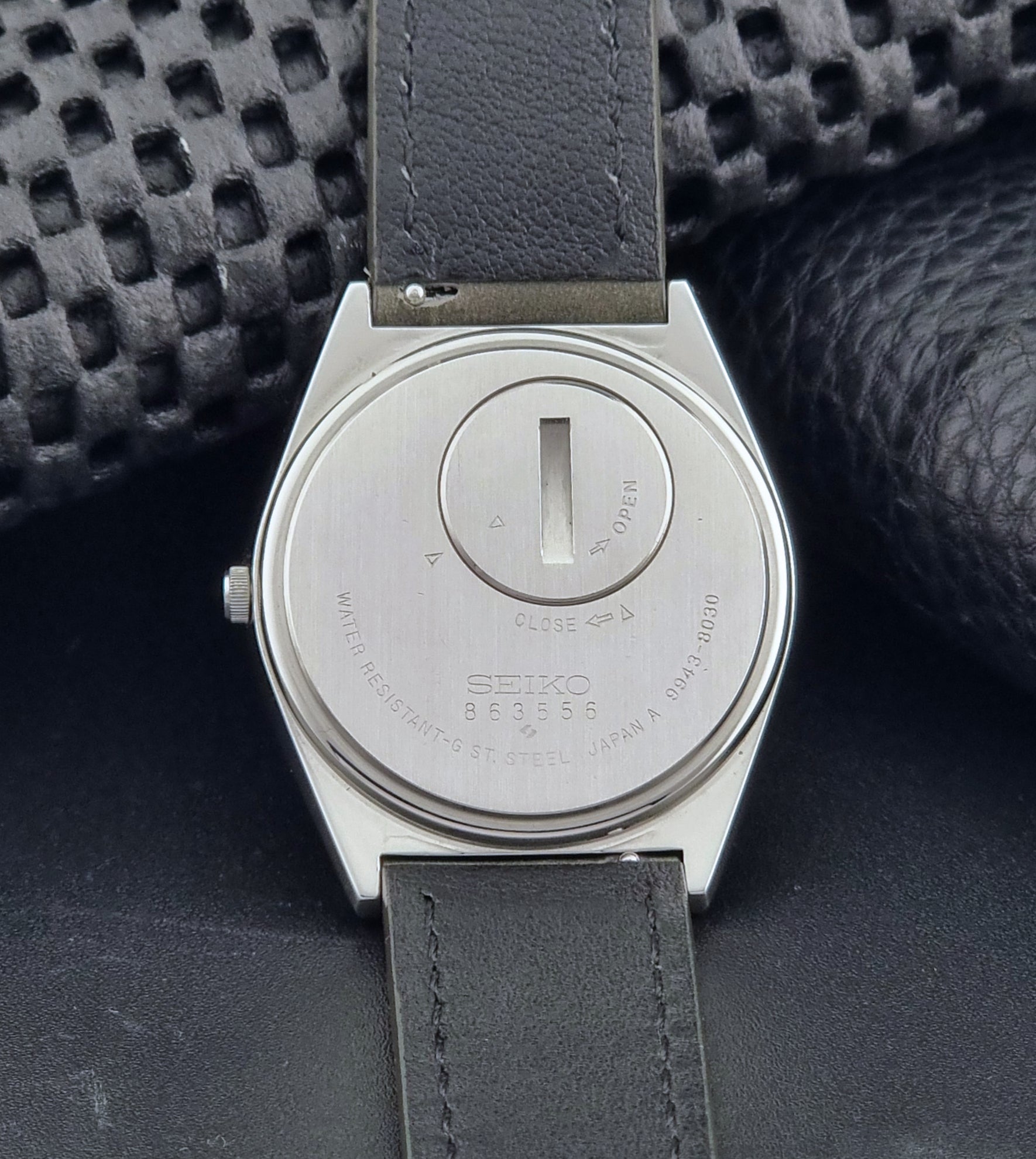Vintage Seiko Grand Quartz watch 9943-8030 with gray leather strap on a dark gray background case back view