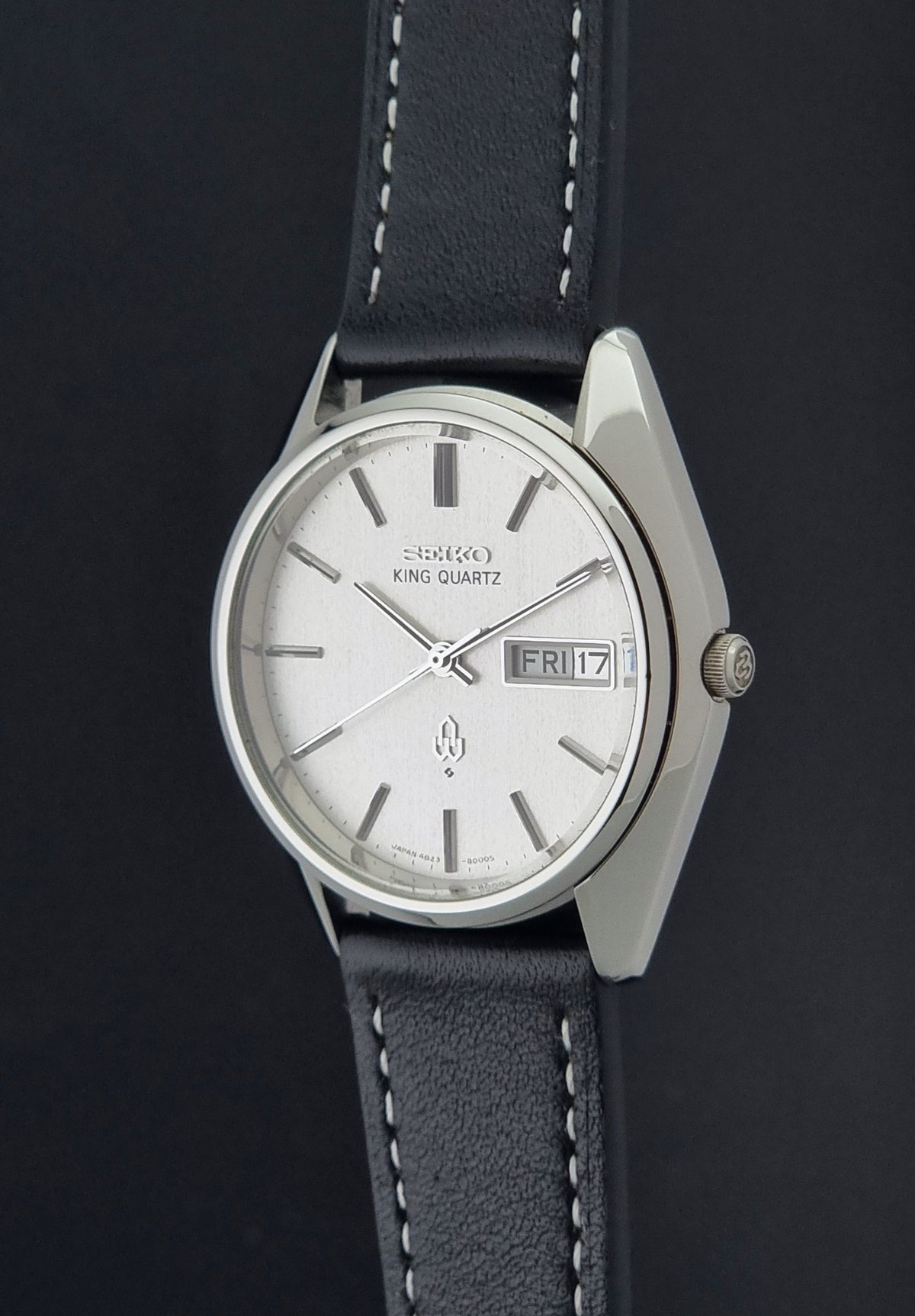 Vintage Seiko King Quartz 4823-8000 watch  with a silver-toned metal case, a white dial, and a dark gray leather strap with white stitching, shown against a dark background.
