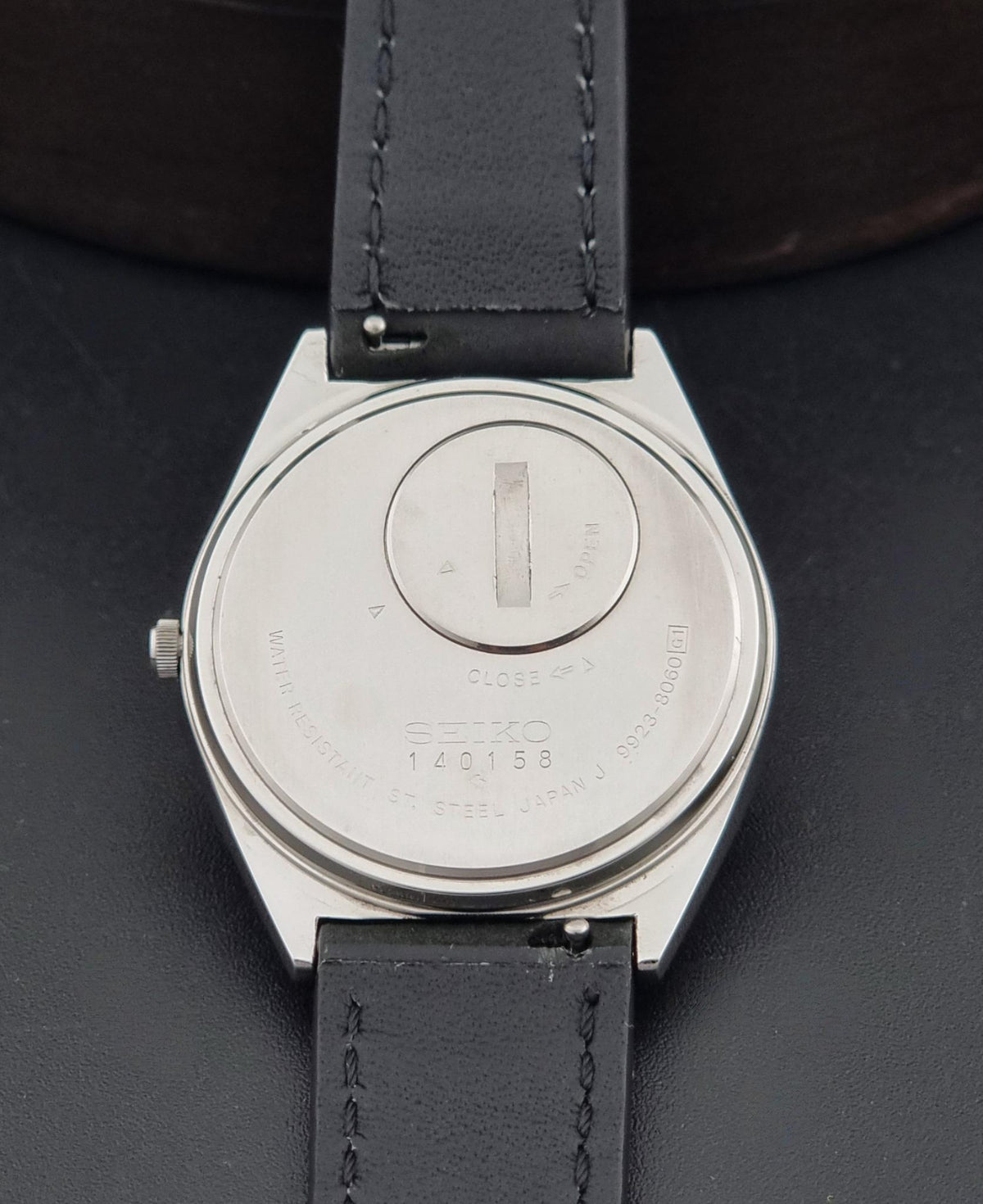 Close-up of the back of a Vintage Seiko King Quartz Wristwatch 9923-8060  watch with a silver-toned metal case and a black leather strap on a dark background.