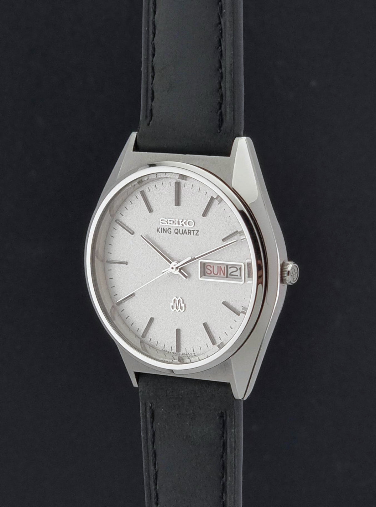 Vintage Seiko King Quartz Wristwatch 9923-8060 watch with a silver-toned metal case, white dial, and black leather strap, shown against a dark background.