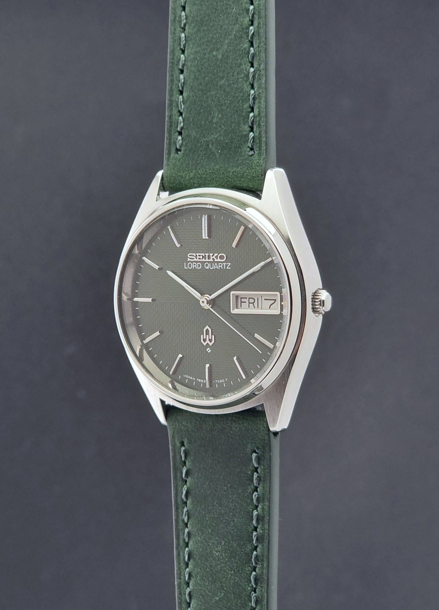 Vintage Seiko Lord Quartz watch 7853-7020 with green strap and silver case on a dark gray background crown profile view
