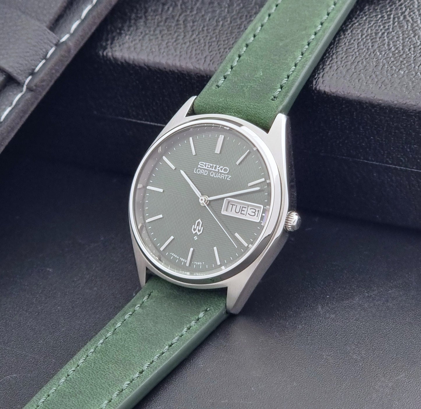 Vintage Seiko Lord Quartz watch 7853-7020 with green strap and silver case on a dark gray background crown view