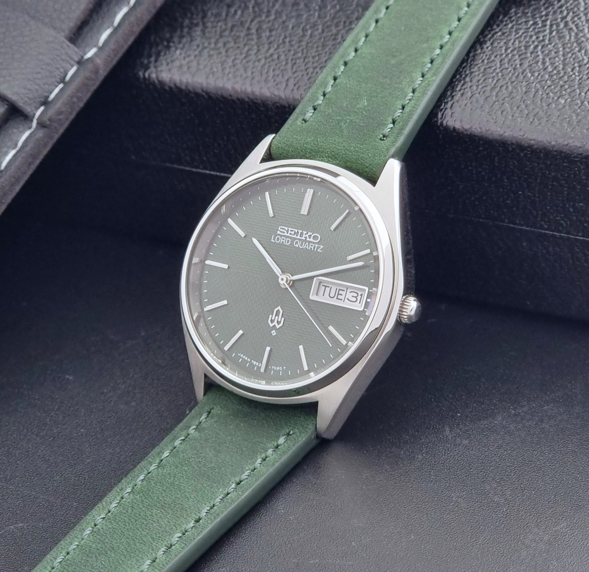 Vintage Seiko Lord Quartz watch 7853-7020 with green strap and silver case on a dark gray background crown view