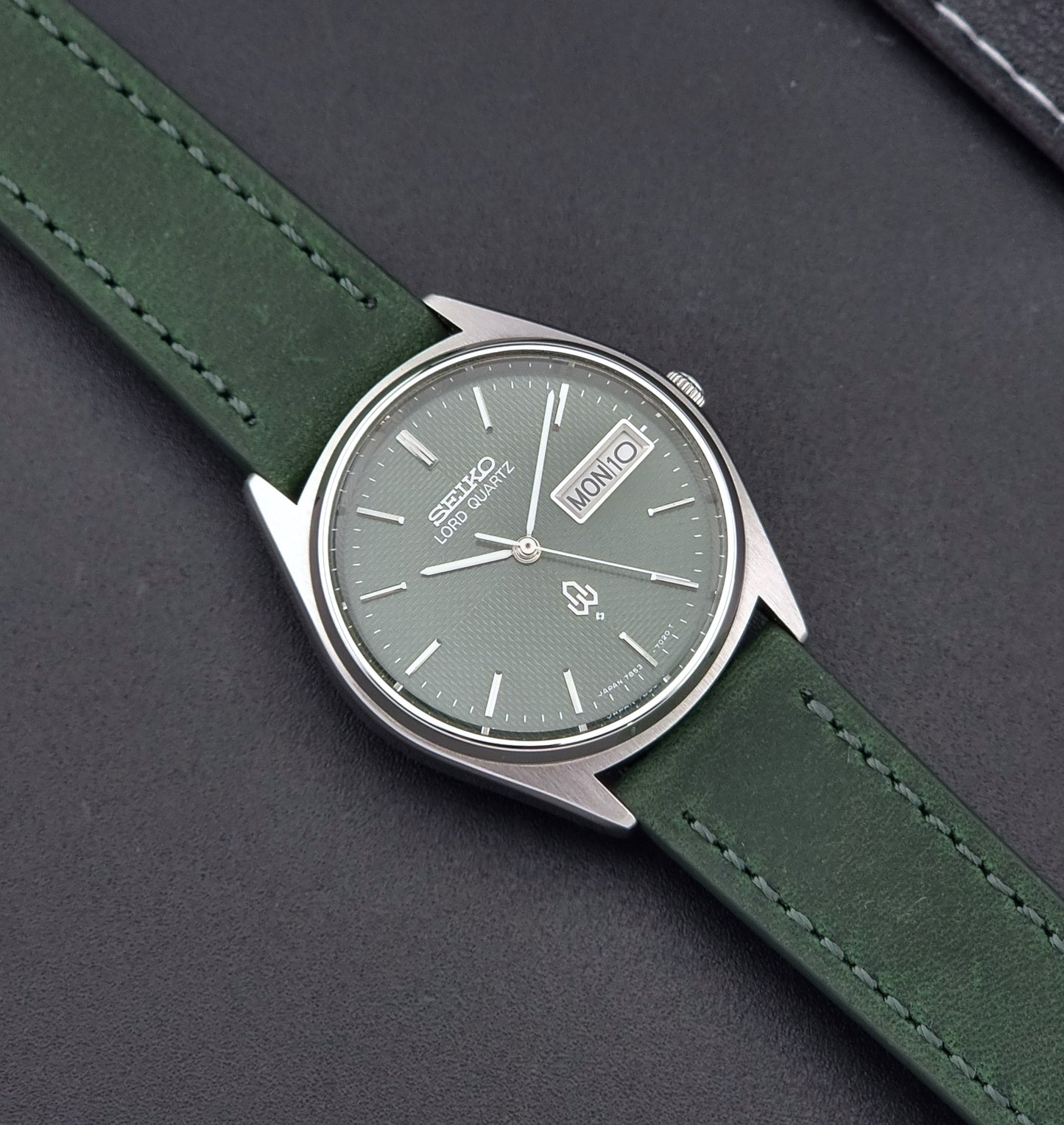 Vintage Seiko Lord Quartz watch 7853-7020 with green strap and silver case on a dark gray background close up dial view