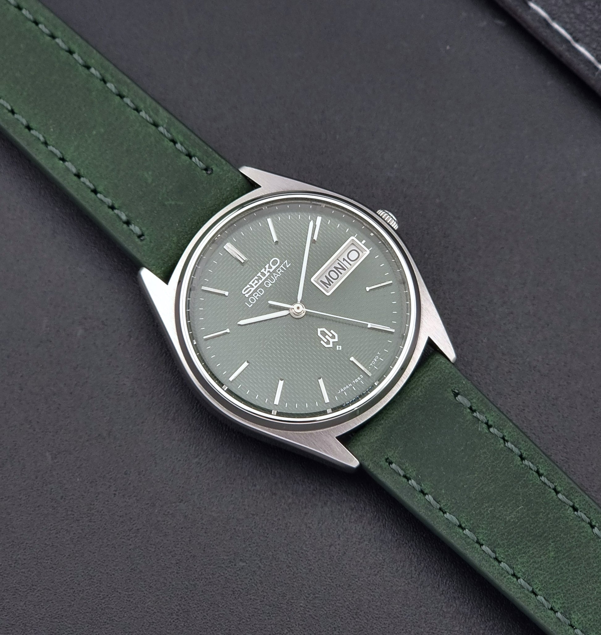 Vintage Seiko Lord Quartz watch 7853-7020 with green strap and silver case on a dark gray background close up dial view