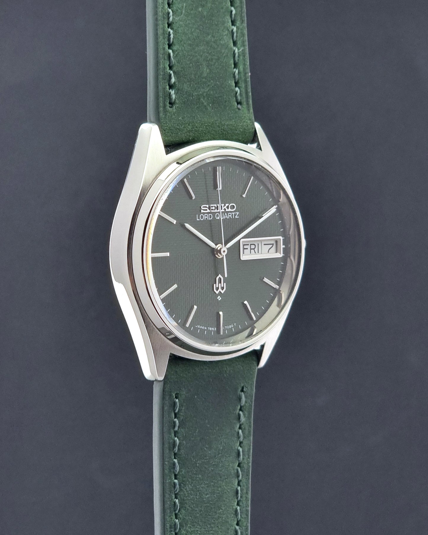 Vintage Seiko Lord Quartz watch 7853-7020 with green strap and silver case on a dark gray background side profile view