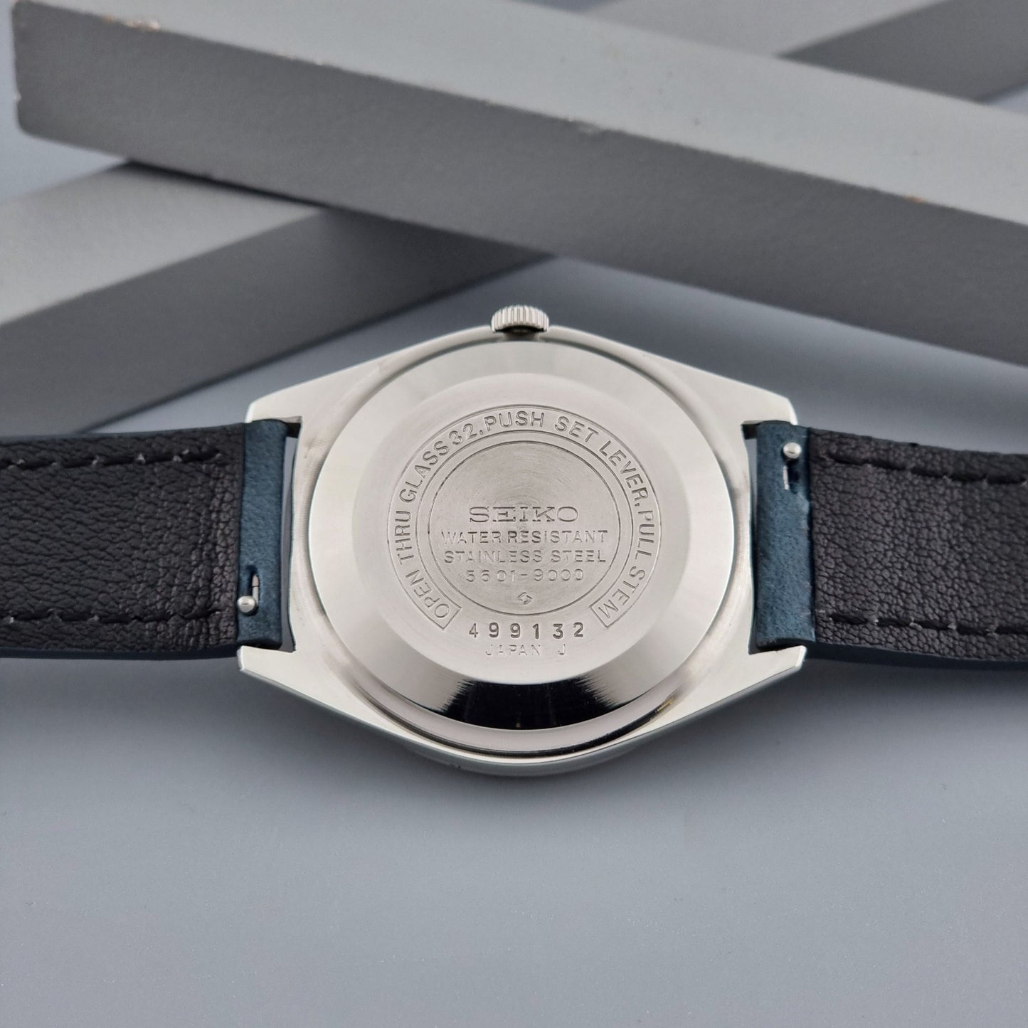 Vintage Seiko Wristwatch LordMatic 5601-9000 with blue strap and silver case on a gray background case back view