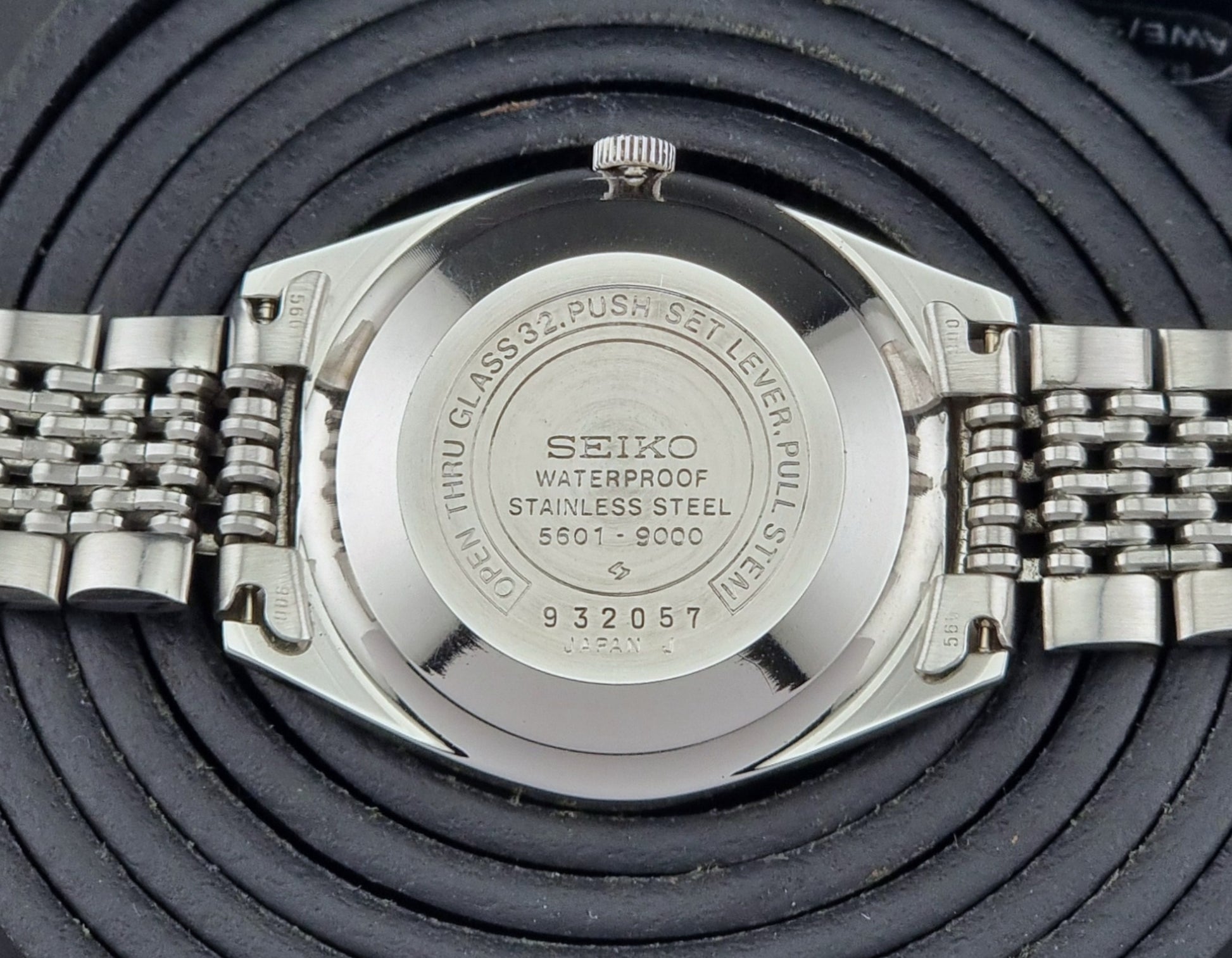 Back view of a Seiko Lord Matic watch with metal band on a textured black background