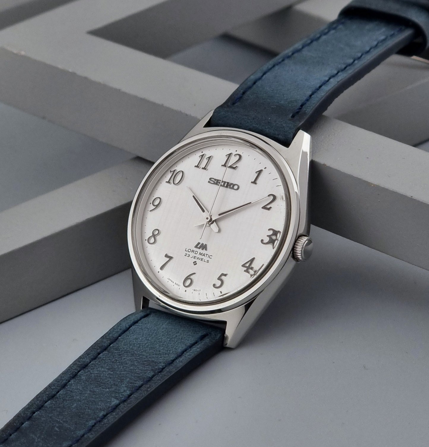 Vintage Seiko Wristwatch LordMatic 5601-9000 with blue strap and silver case on a gray background crown view