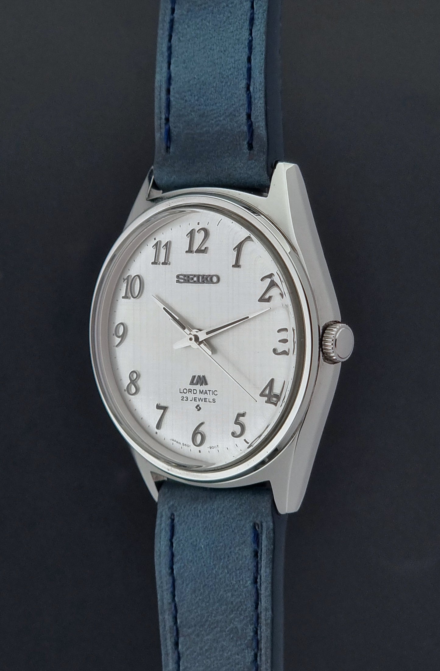 Vintage Seiko Wristwatch LordMatic 5601-9000 with blue strap and silver case on a gray background side crown view