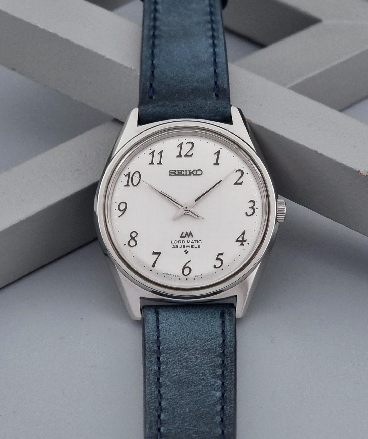 Vintage Seiko Wristwatch LordMatic 5601-9000 with blue strap and silver case on a gray background front view