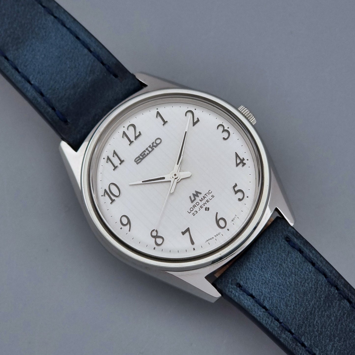 Vintage Seiko Wristwatch LordMatic 5601-9000 with blue strap and silver case on a gray background close dial view