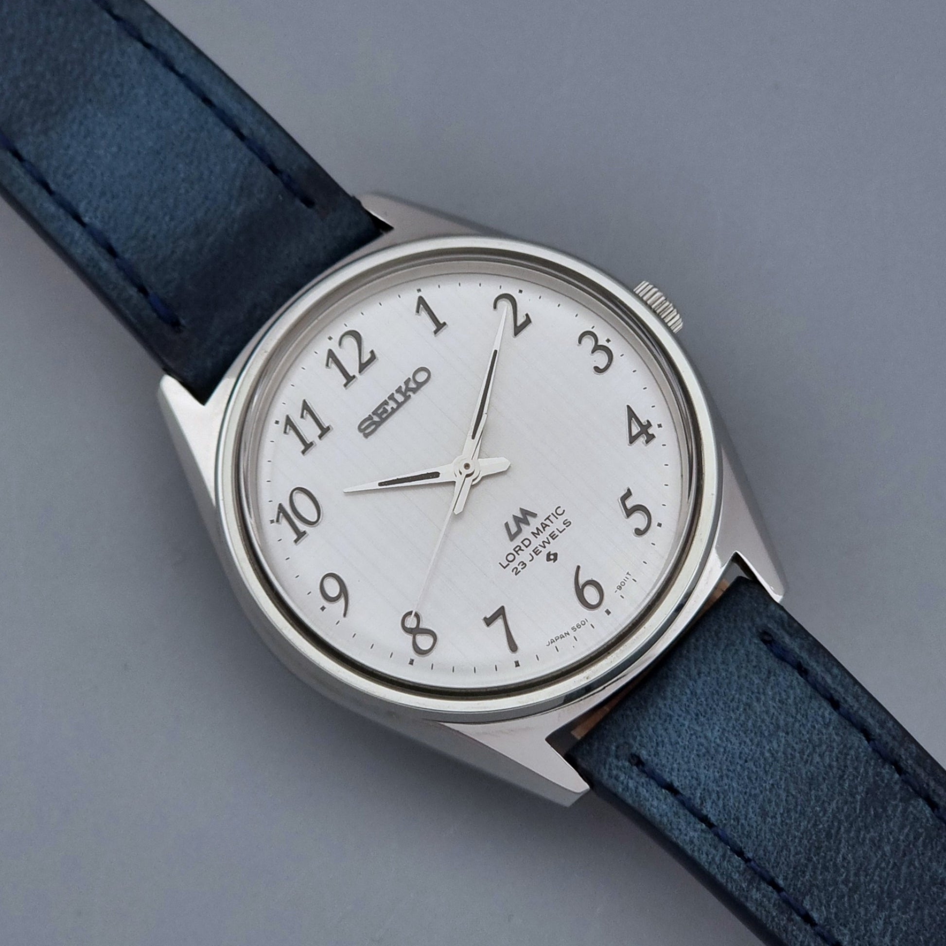 Vintage Seiko Wristwatch LordMatic 5601-9000 with blue strap and silver case on a gray background close dial view