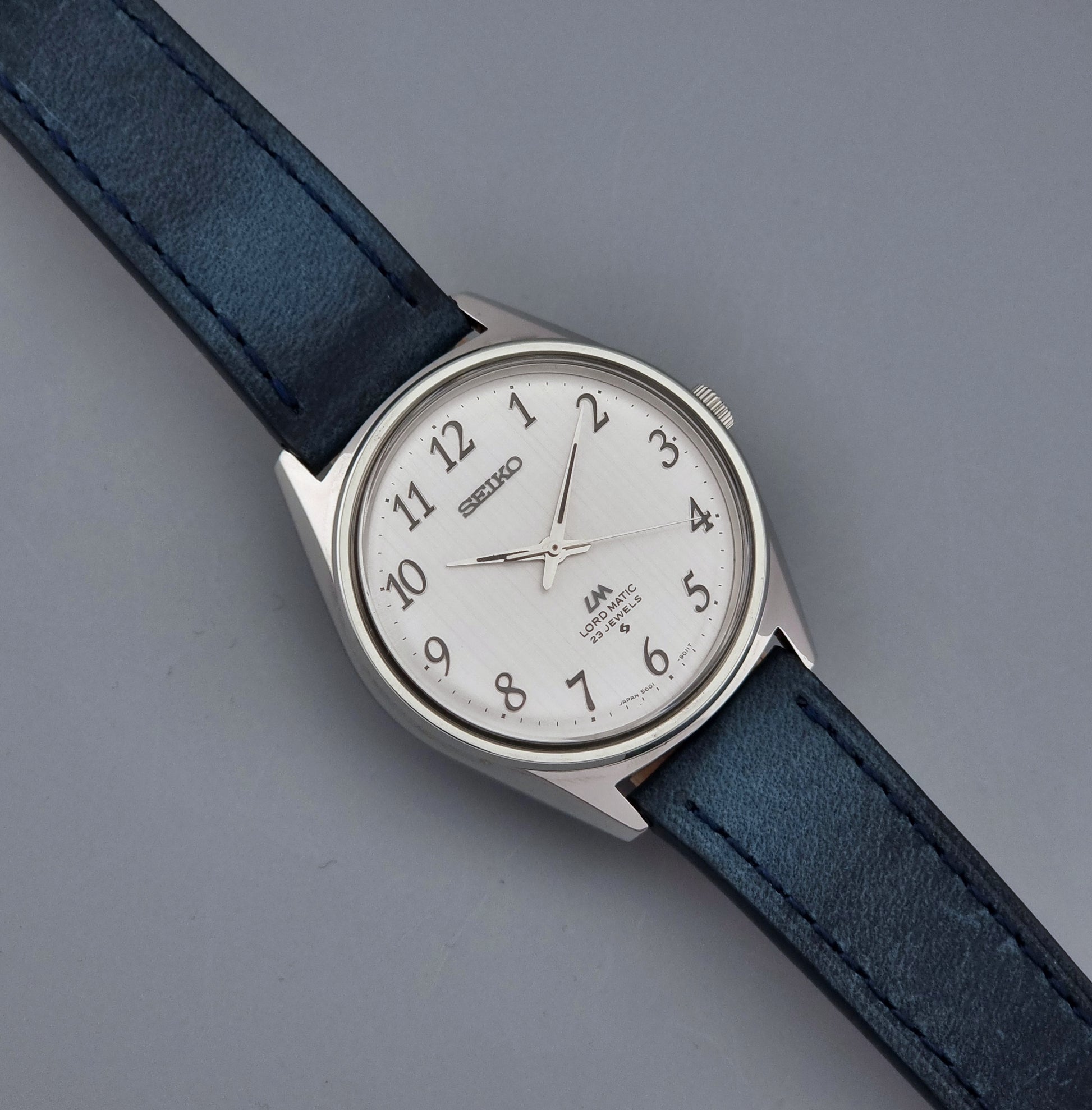 Vintage Seiko Wristwatch LordMatic 5601-9000 with blue strap and silver case on a gray background front