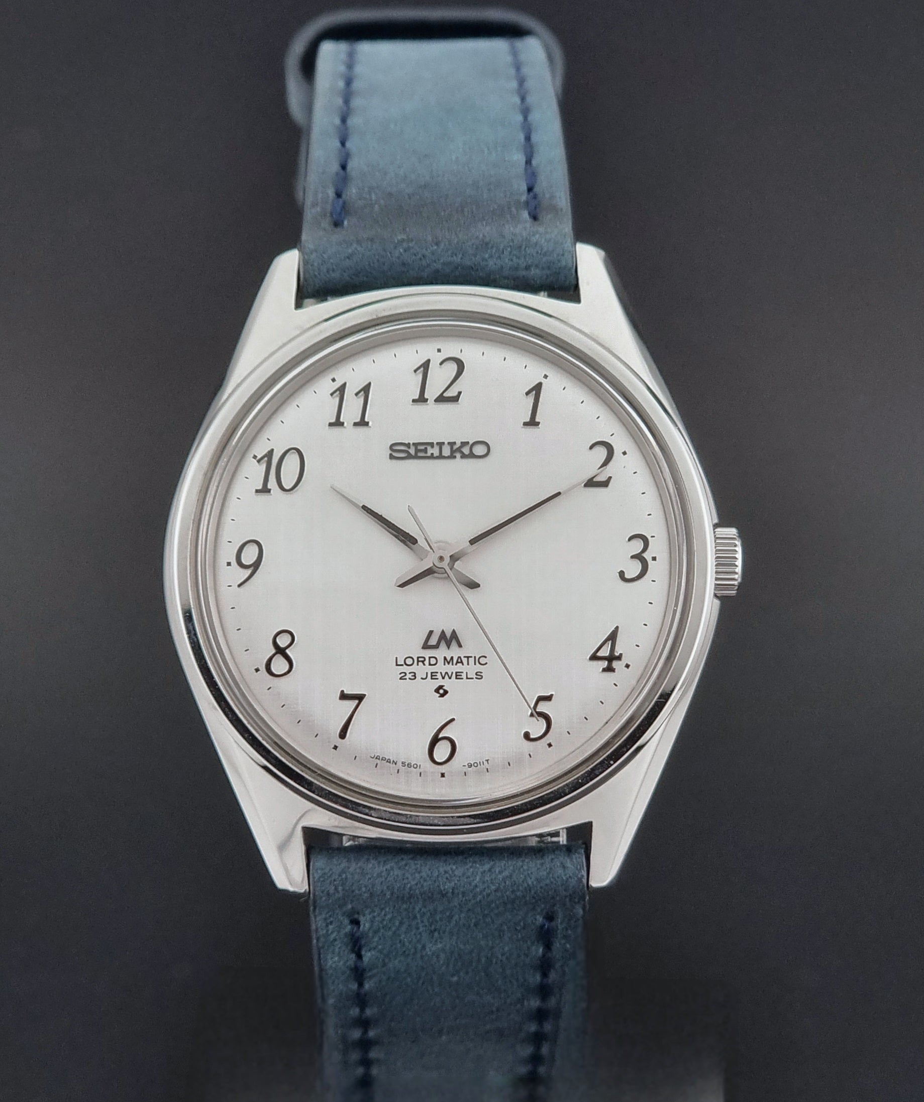 Vintage Seiko Wristwatch LordMatic 5601-9000 with blue strap and silver case on a gray background dial view