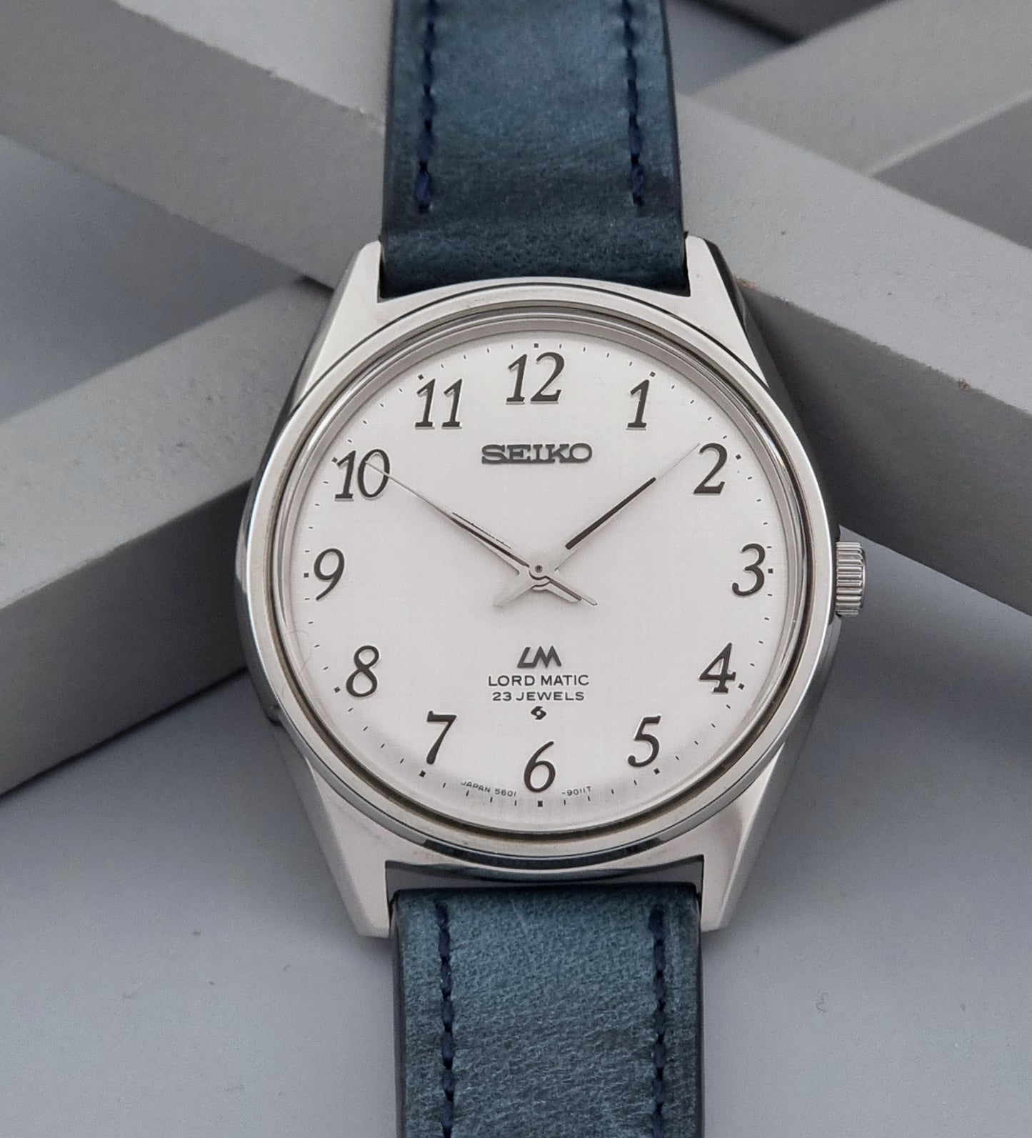 Vintage Seiko Wristwatch LordMatic 5601-9000 with blue strap and silver case on a gray background close up dial view