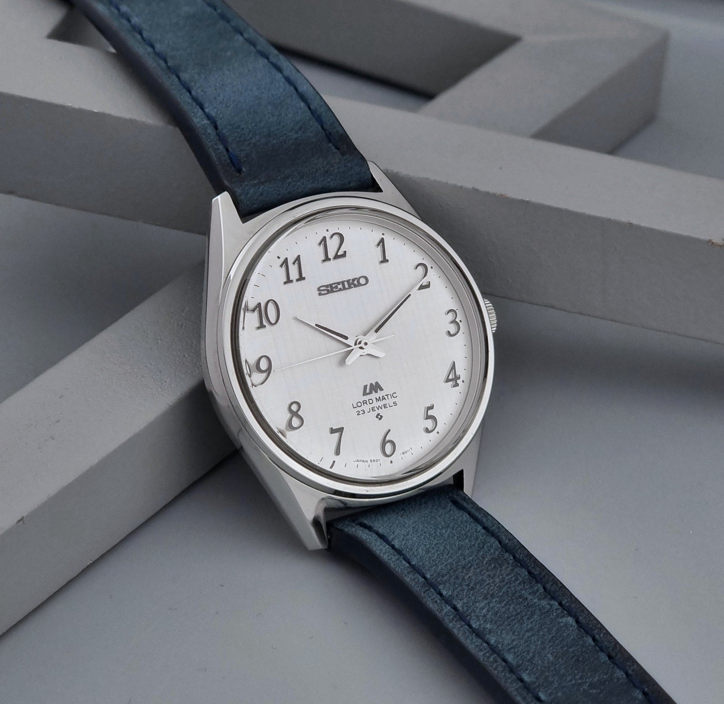 Vintage Seiko Wristwatch LordMatic 5601-9000 with blue strap and silver case on a gray background side view