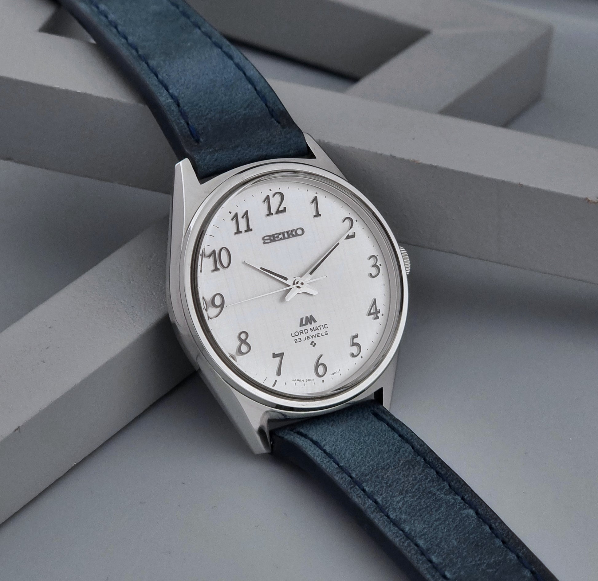 Vintage Seiko Wristwatch LordMatic 5601-9000 with blue strap and silver case on a gray background side view